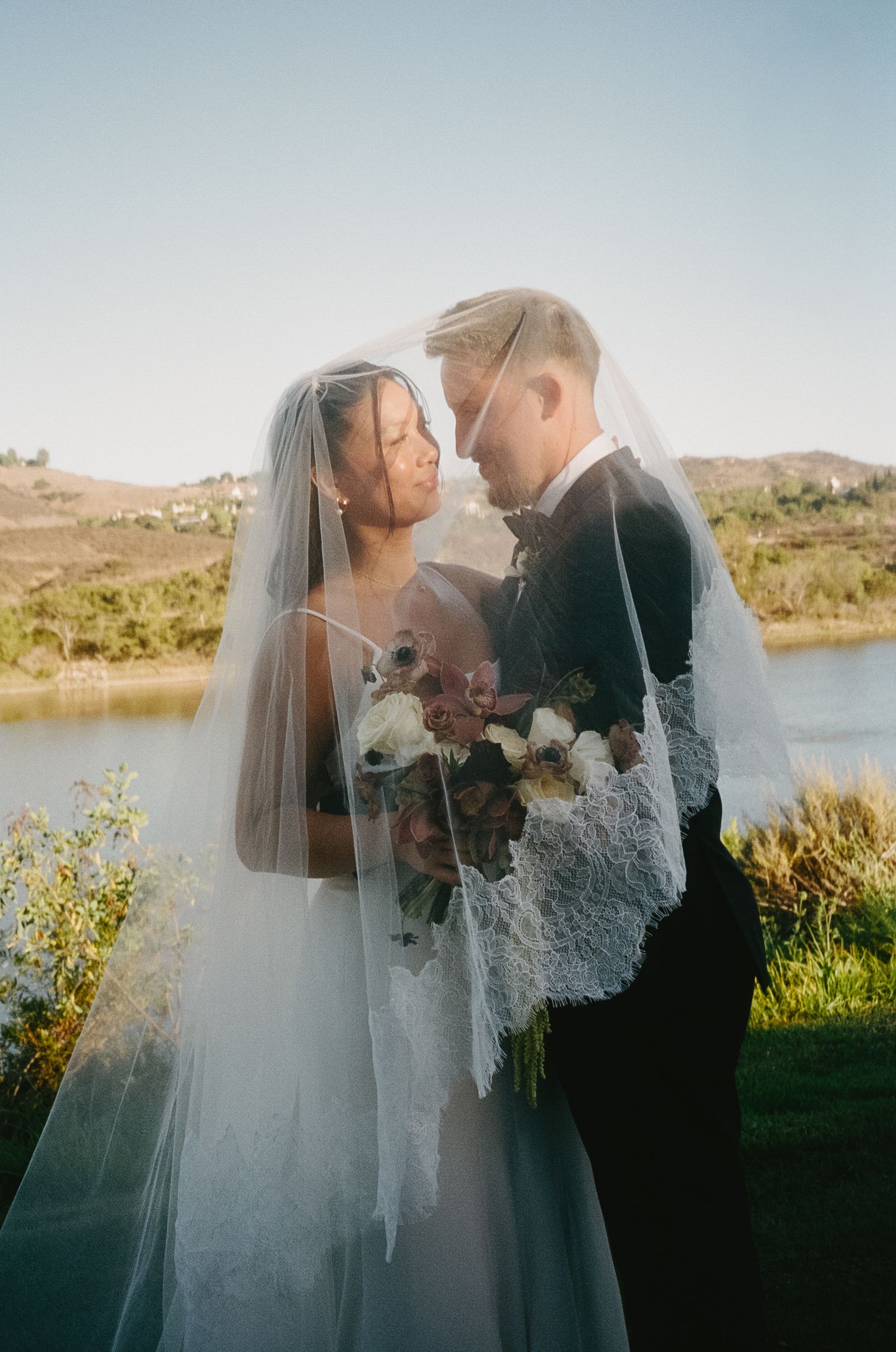 Romantic lakeside wedding portrait with couple embracing against natural scenery.
