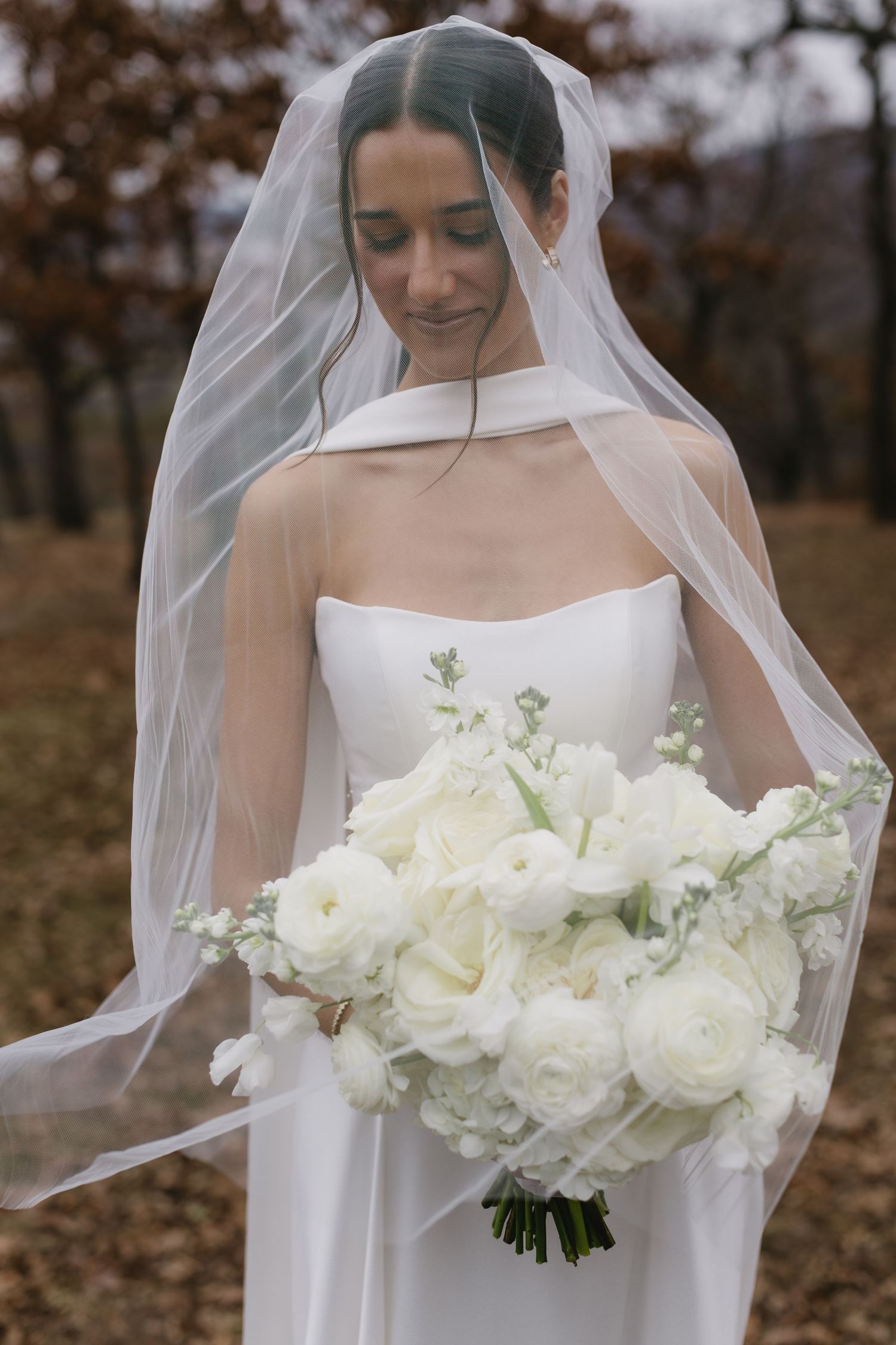 Bride in white dress holding classic white rose bouquet during autumn outdoor wedding.
