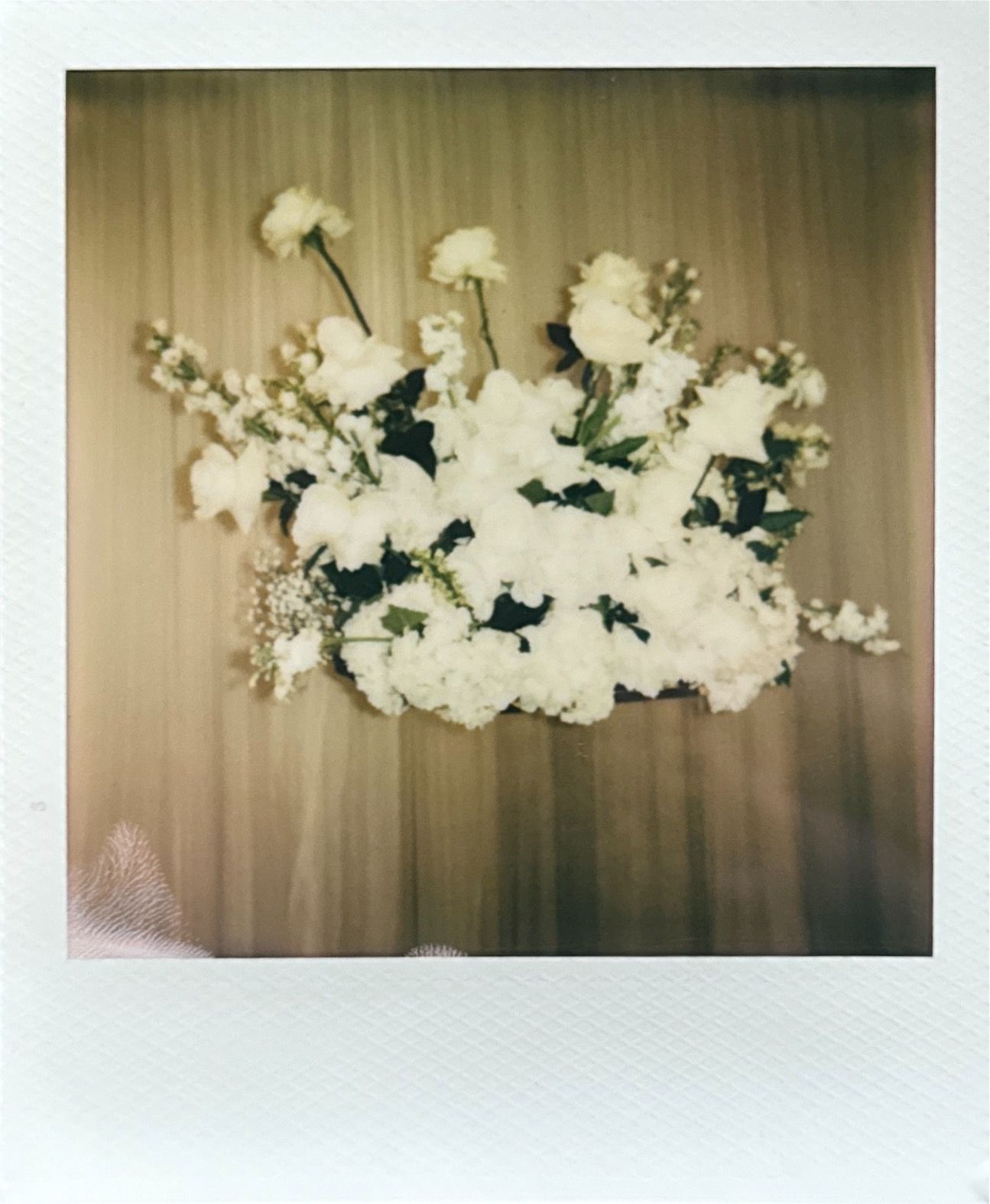 White floral wedding arch arrangement against neutral backdrop.