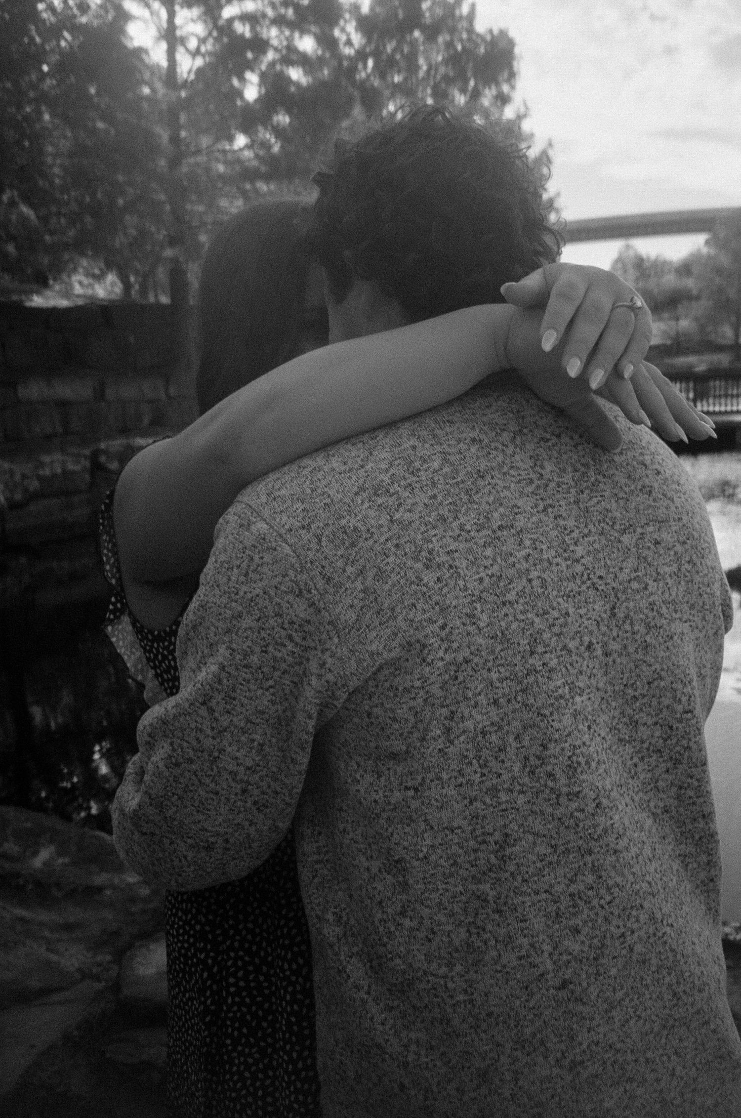 A black and white photo capturing a tender embrace between two people outdoors.