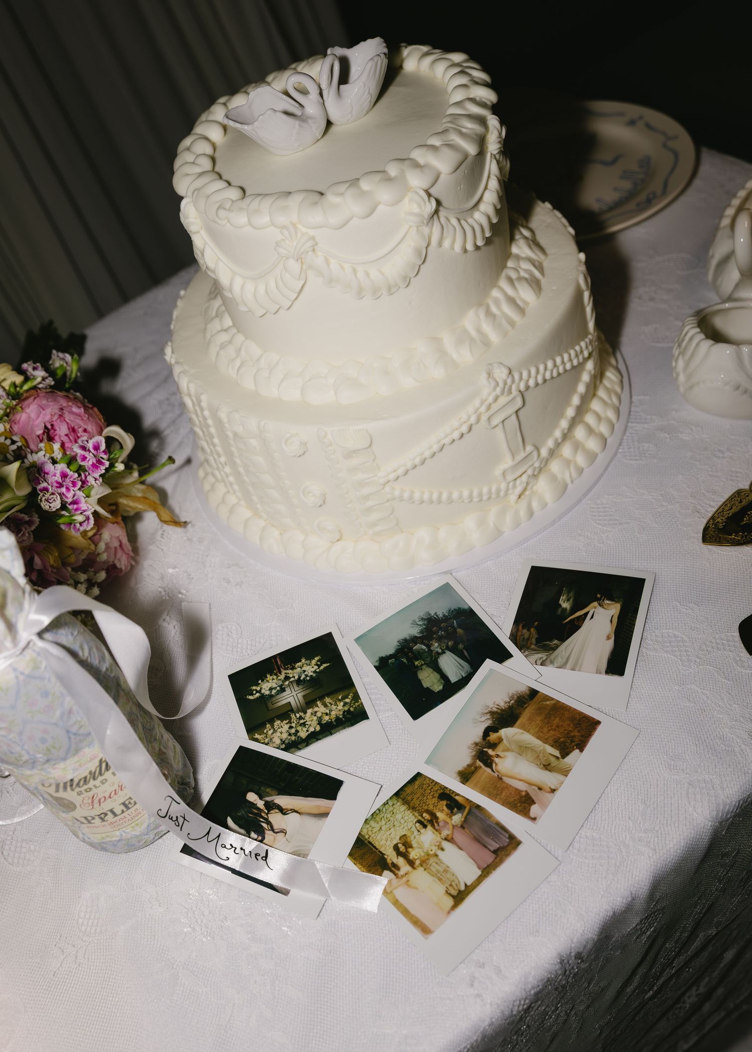 White wedding cake on a table with vintage photographs and small floral arrangements displayed beneath it.