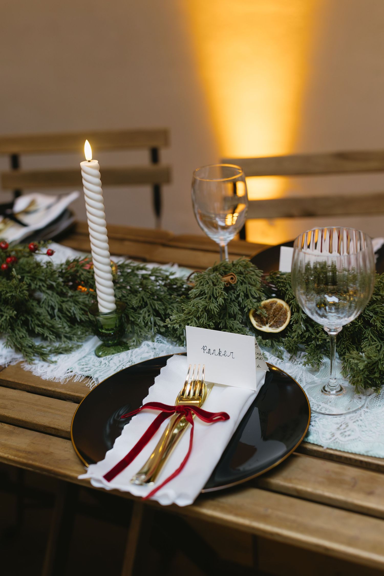 Elegant holiday table setting with candle, greenery and wine glasses.