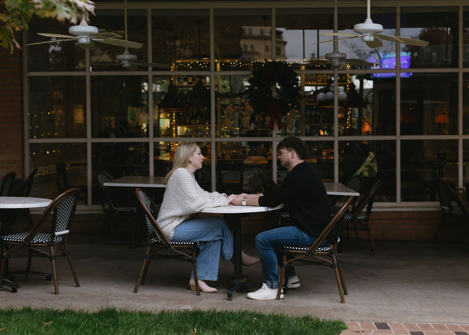 A couple sitting at an outdoor cafe table having a conversation.