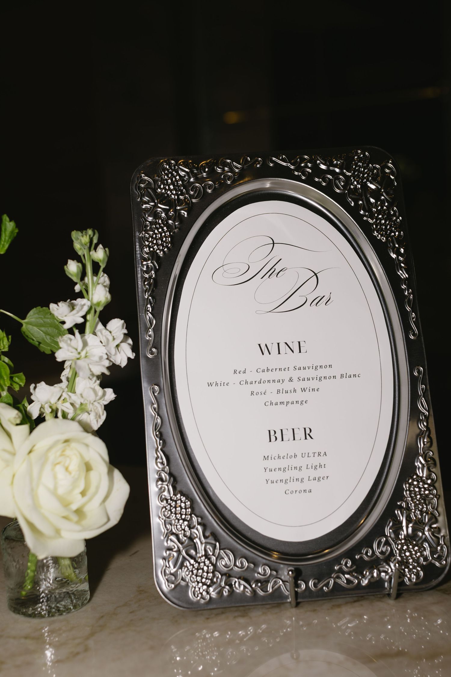Wedding bar menu signs in silver frames with white floral decorations.