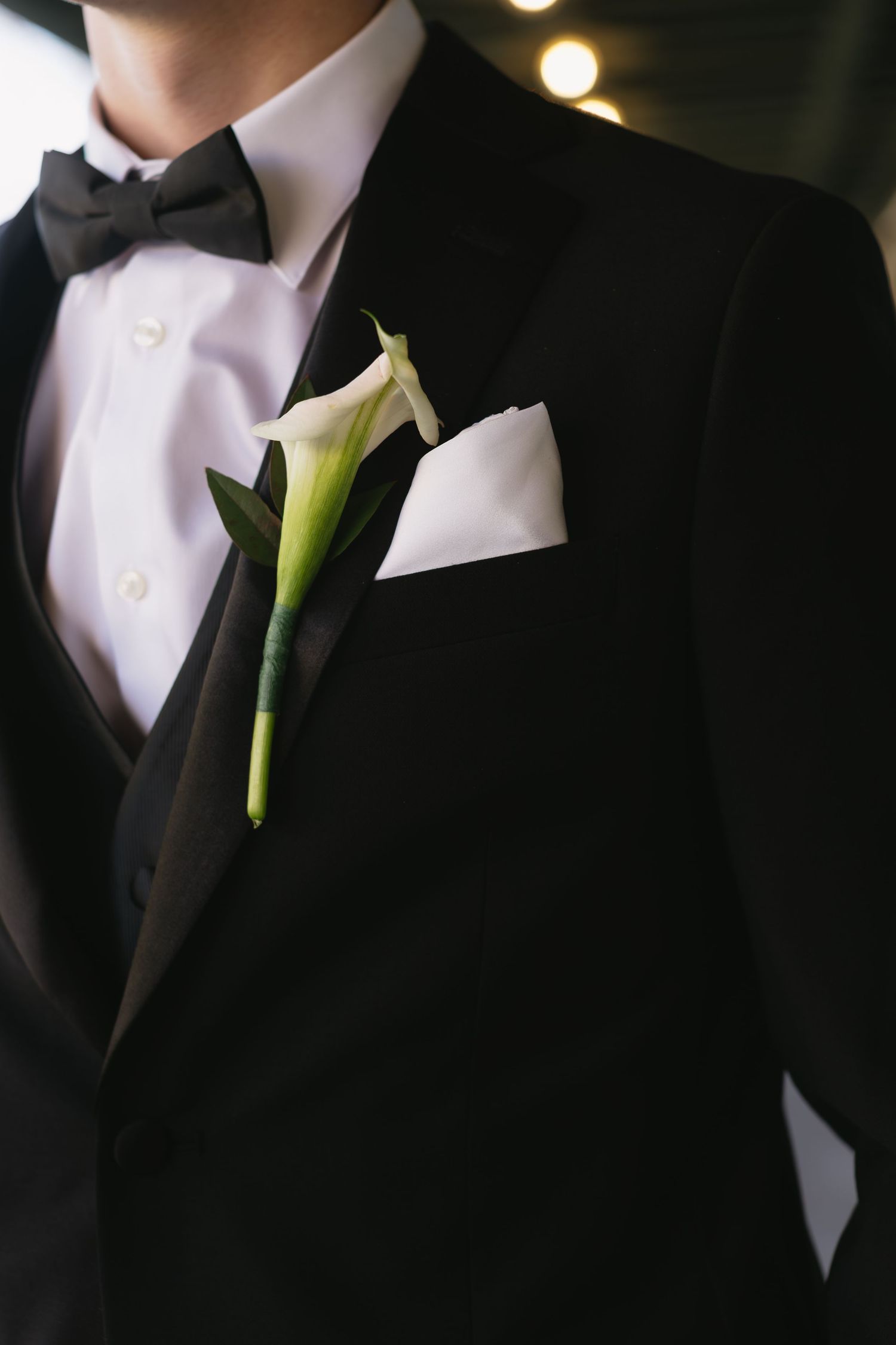 Close-up details of black tuxedos with white calla lily boutonnieres.