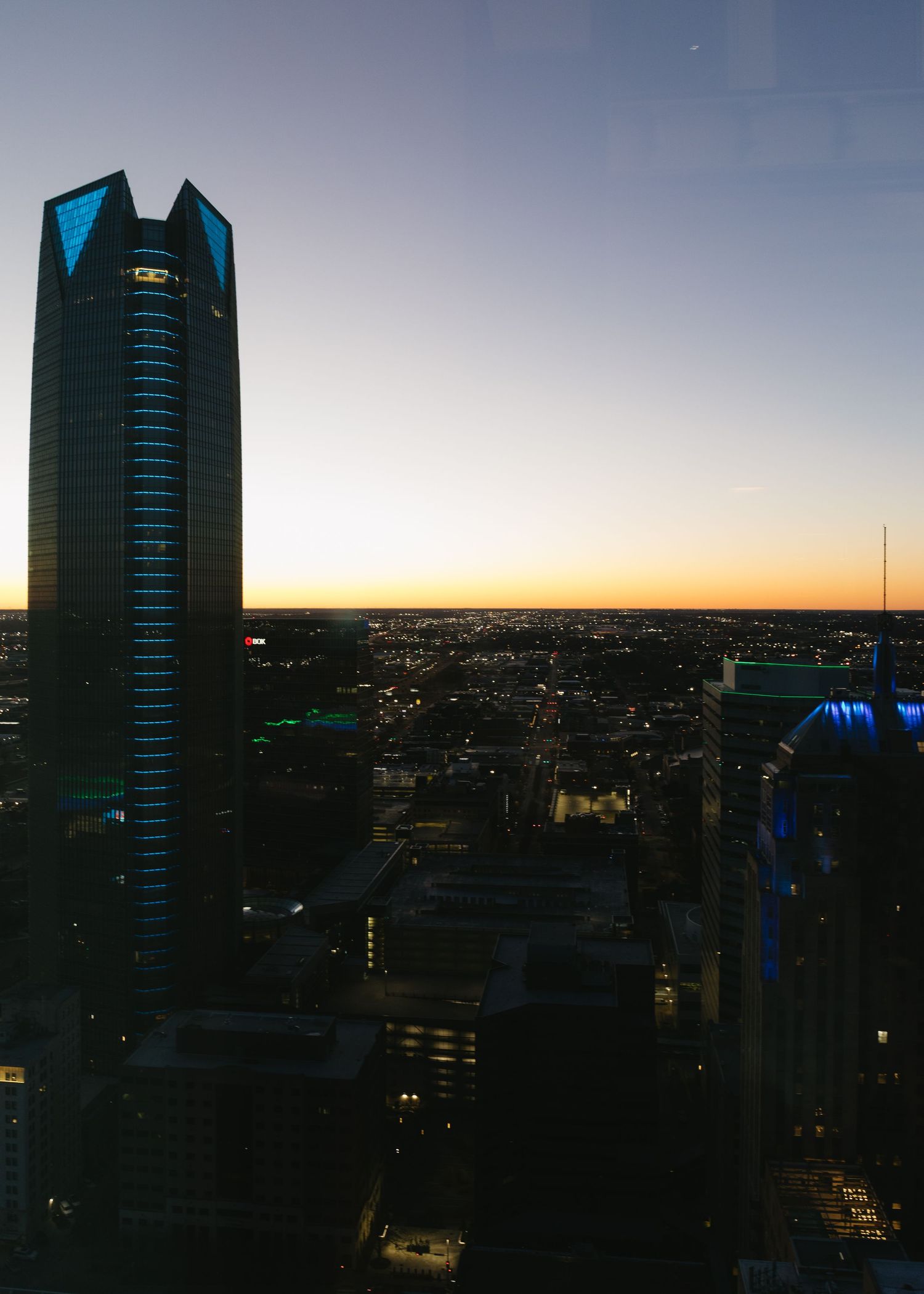 City skyline at dusk with silhouetted office buildings against an orange sunset sky.