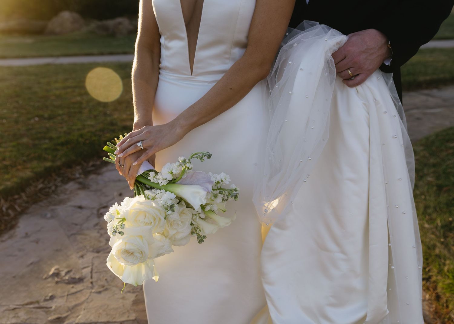 Detail shot of white wedding dress and bouquet in natural sunlight.