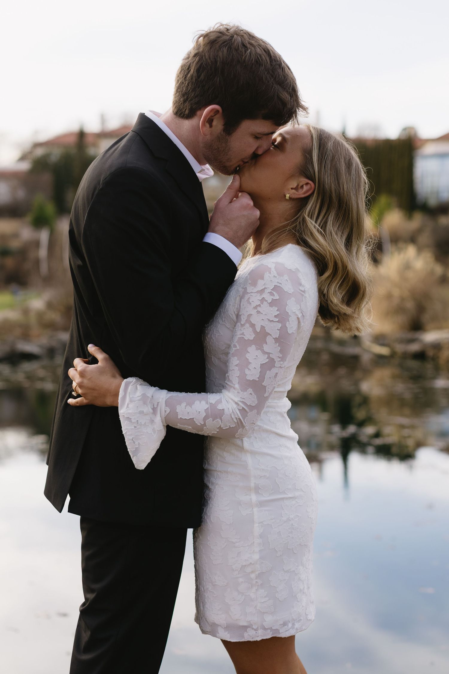 A couple shares intimate moments by a reflective lake during a photo session.