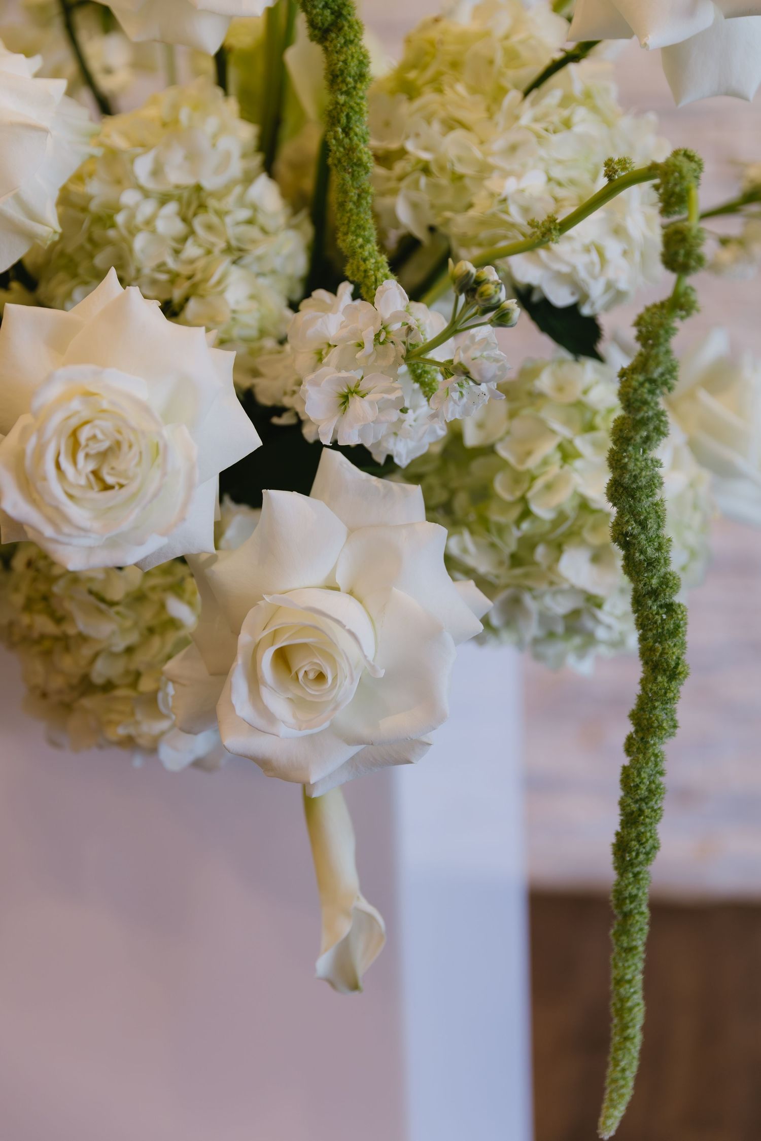 Elegant white floral centerpiece with roses and hydrangeas in tall white vases against a soft background.