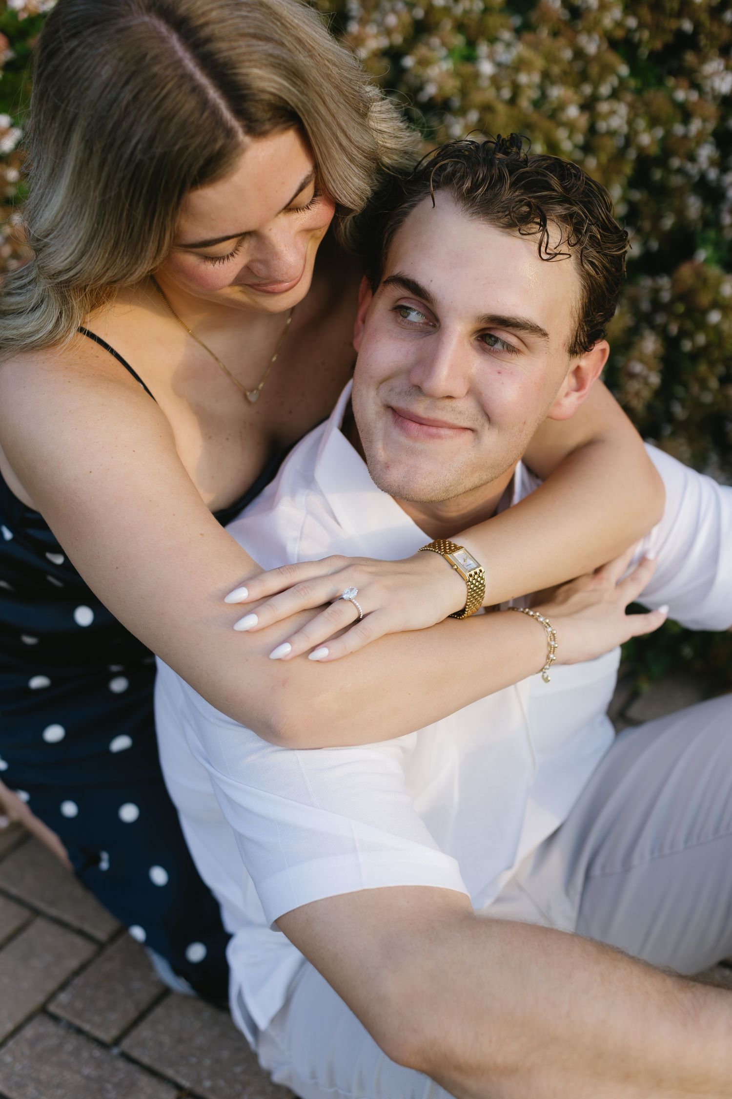 A couple shares a tender embrace while sitting together, with one wearing polka dots and the other in white.