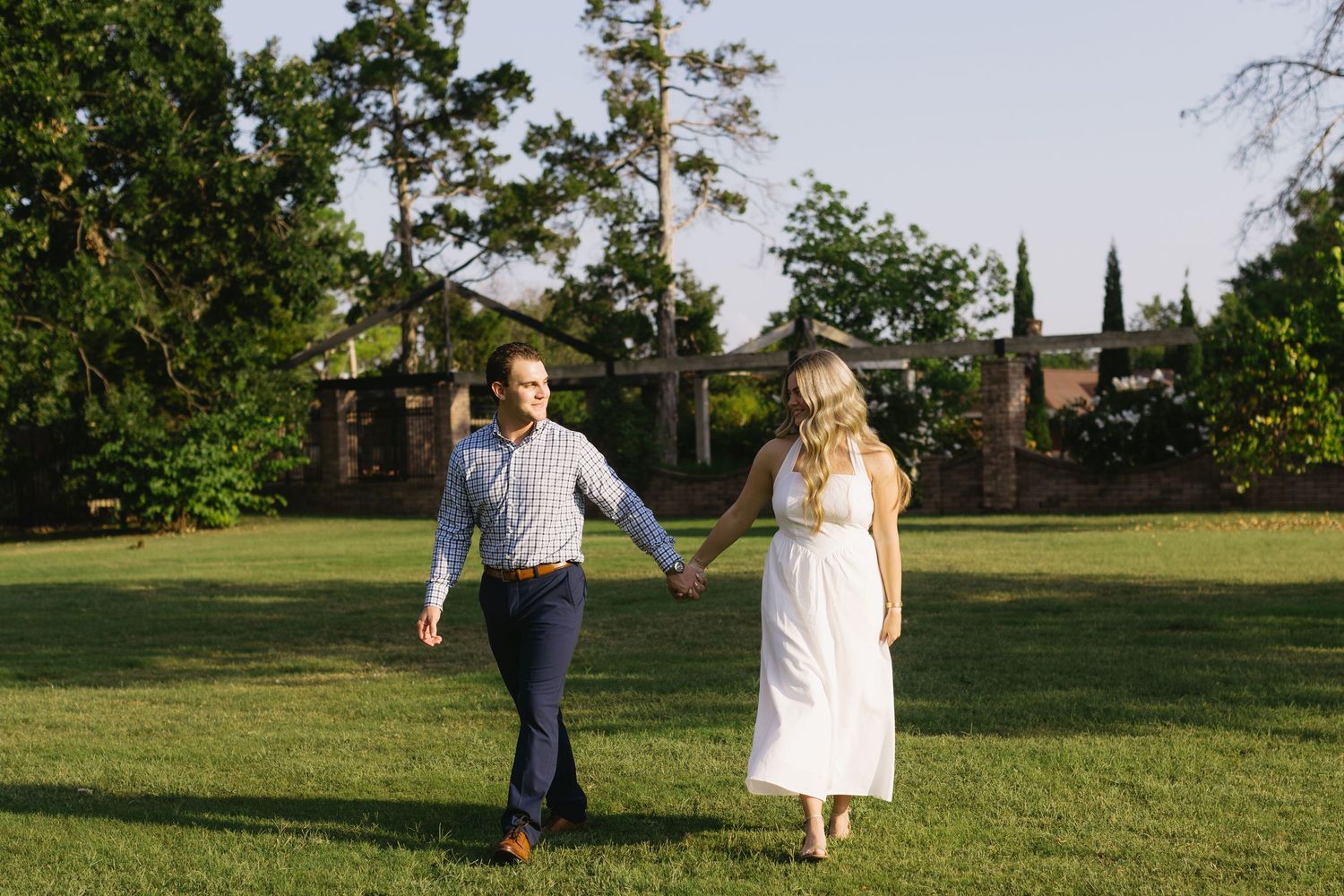 Romantic couple walks together across a lush green field on a sunny afternoon.