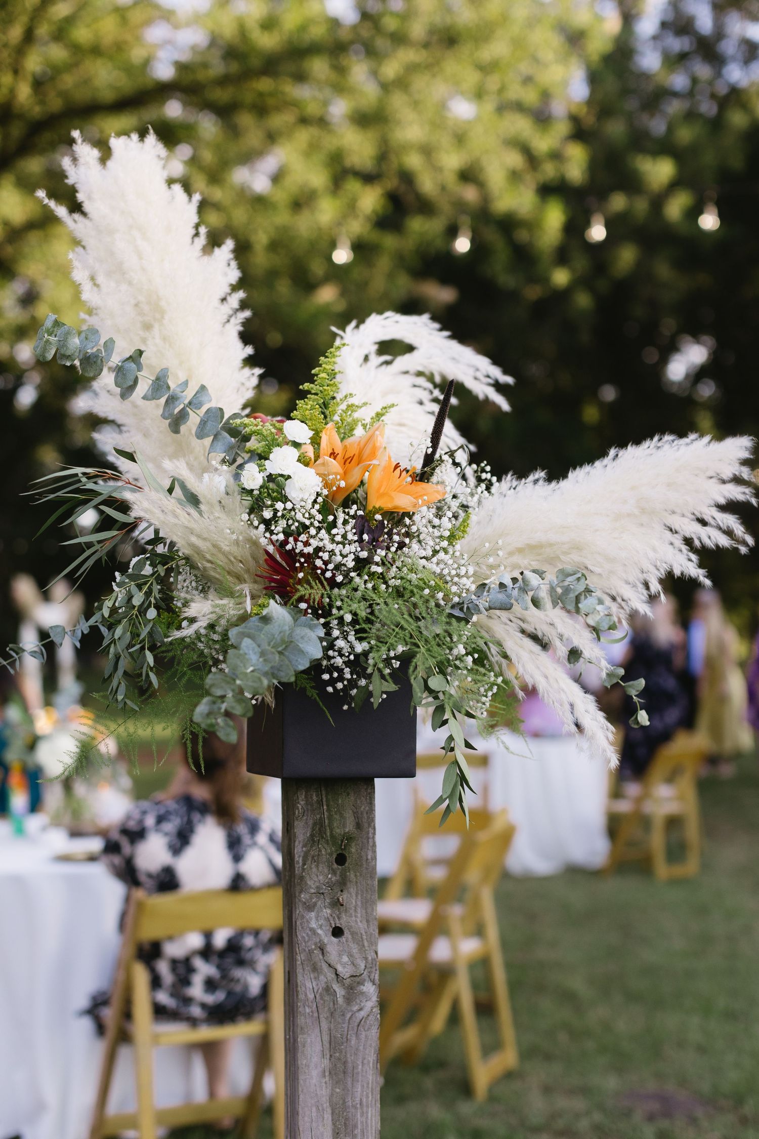 White pampas grass and floral decorations on rustic wooden posts create a romantic outdoor wedding aisle.
