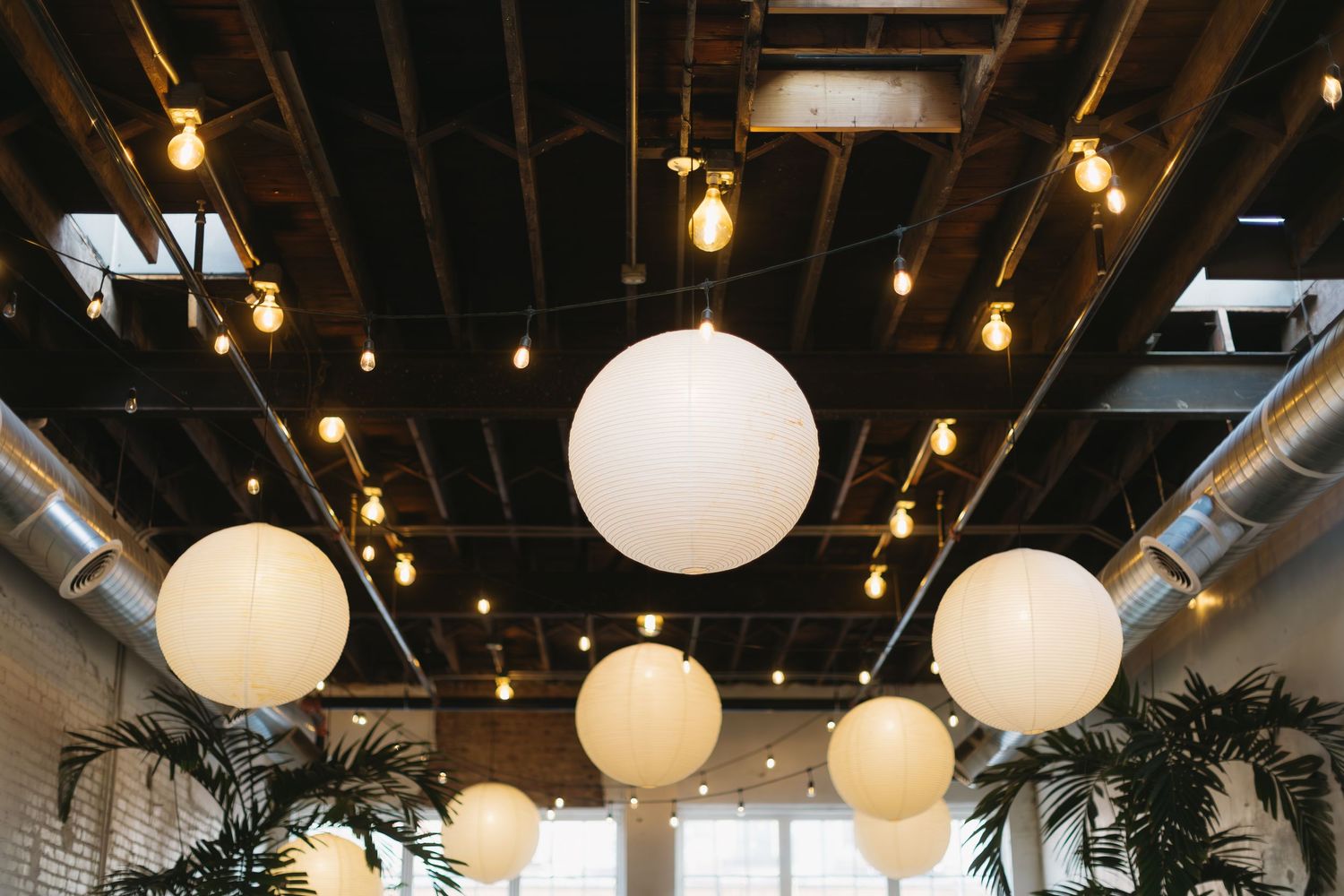 Modern restaurant interior with round white pendant lights and dark exposed ceiling beams creates an industrial-chic ambiance.