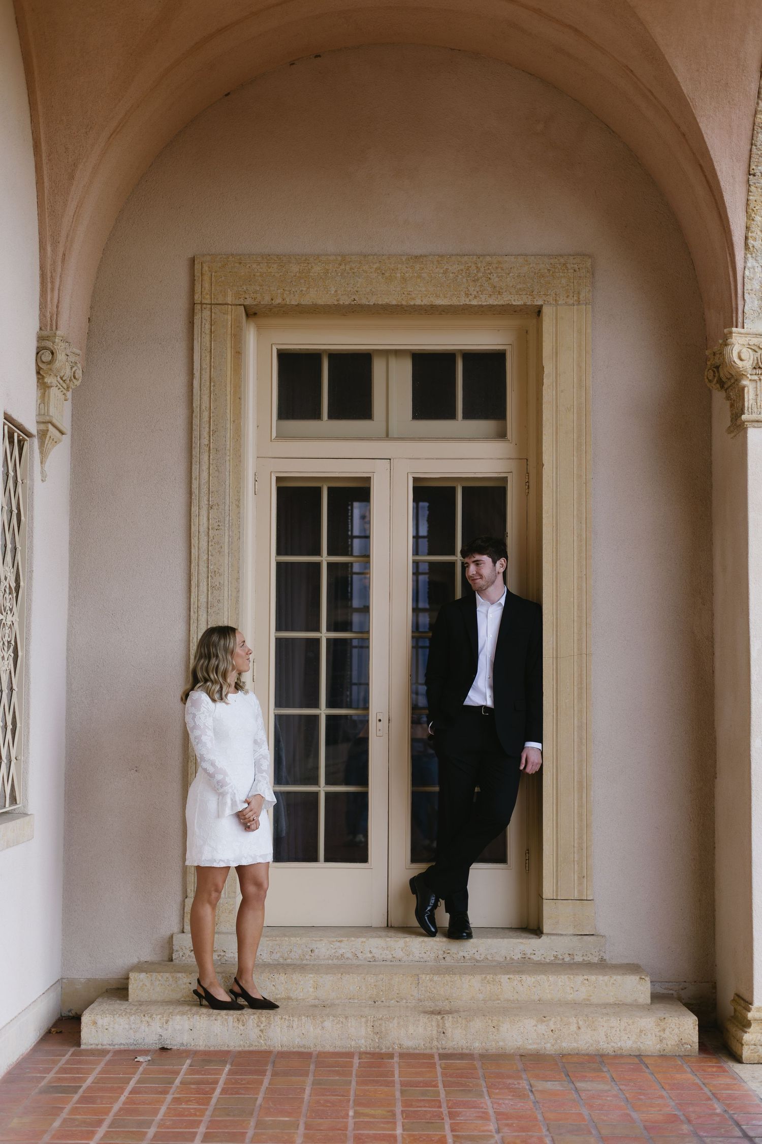 A couple in formal wear standing in an elegant archway with French doors.