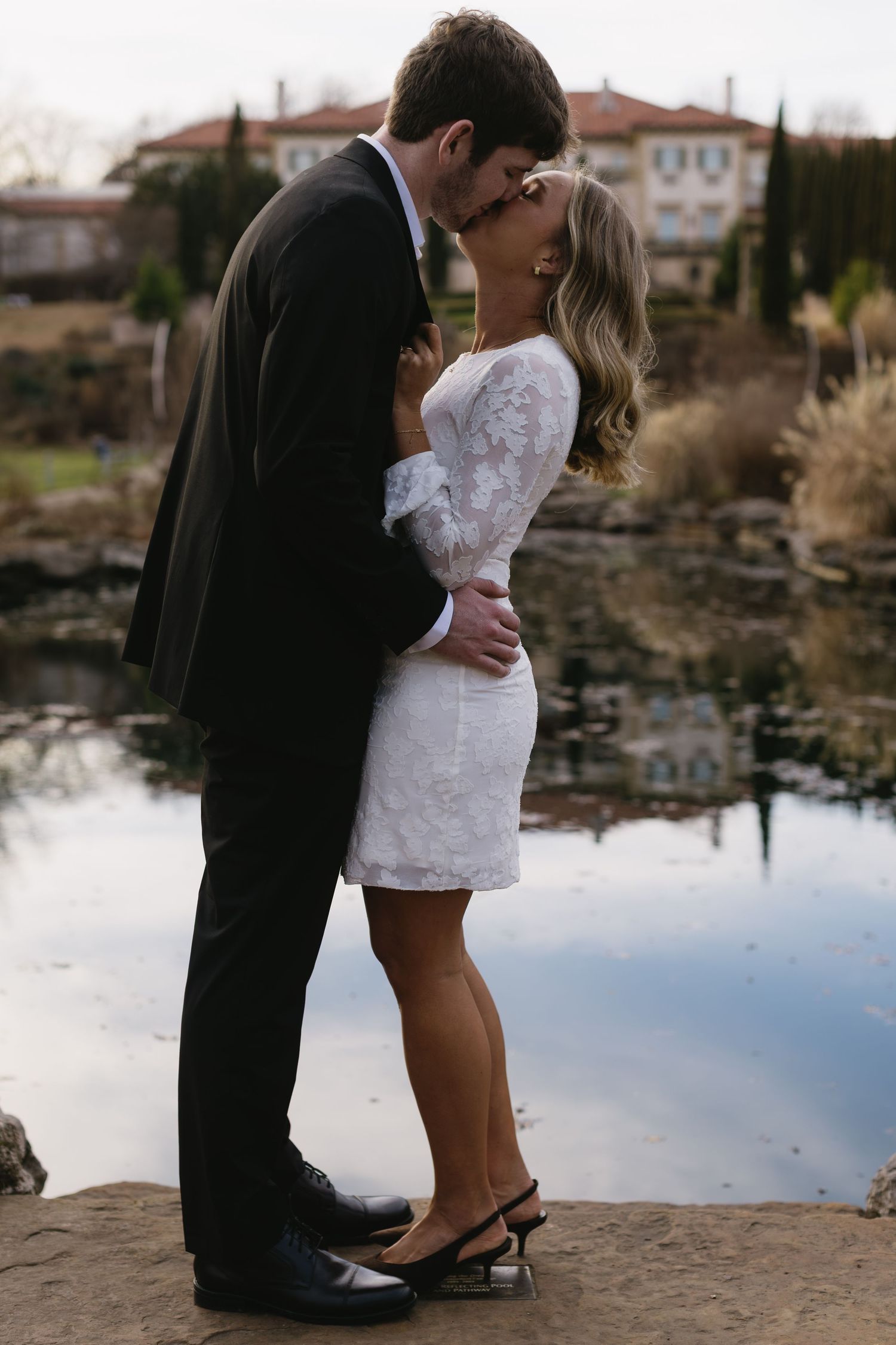 A romantic lakeside moment with water reflections and buildings in the distance.
