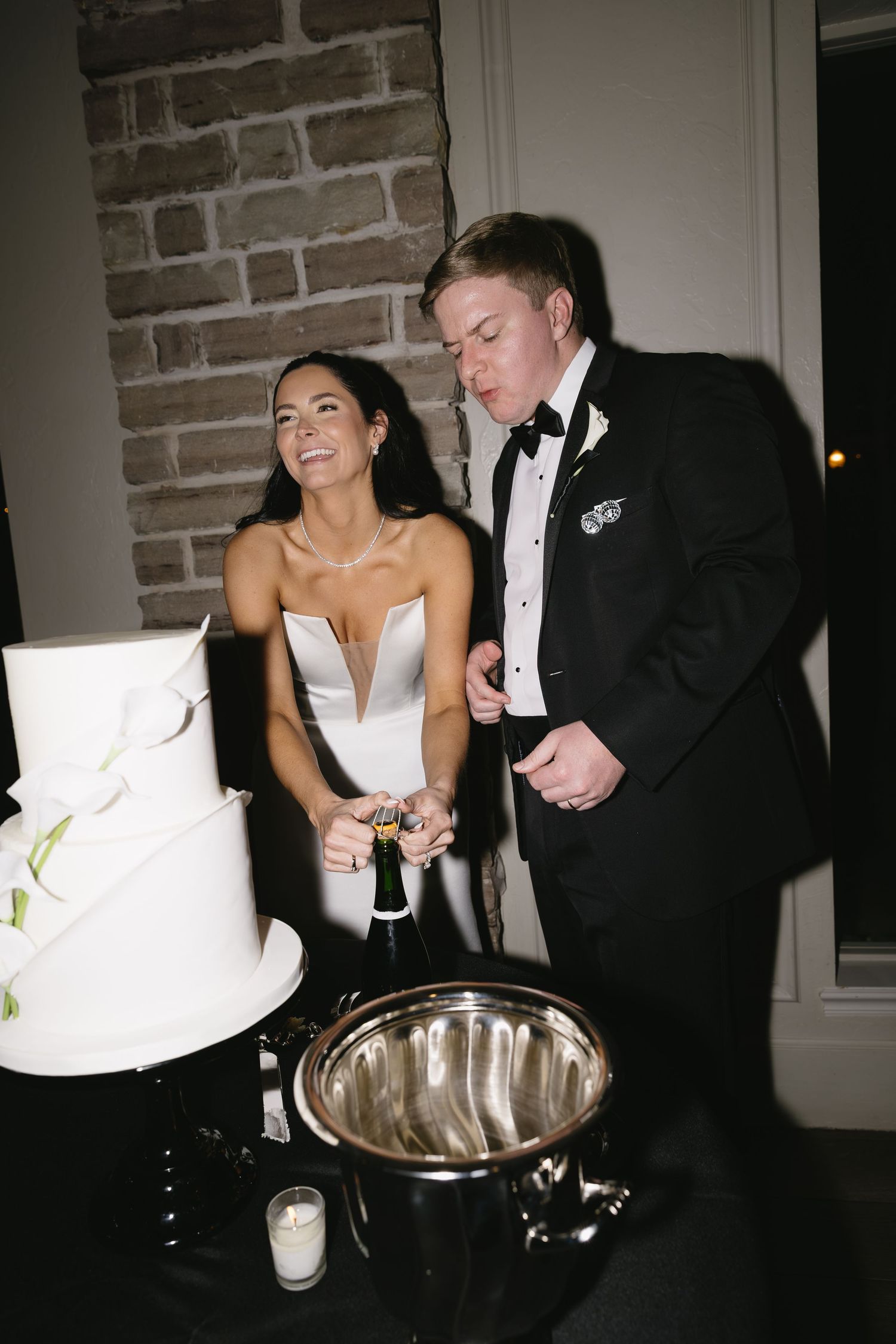 A couple shares a joyful moment during their wedding reception next to a silver champagne bucket.