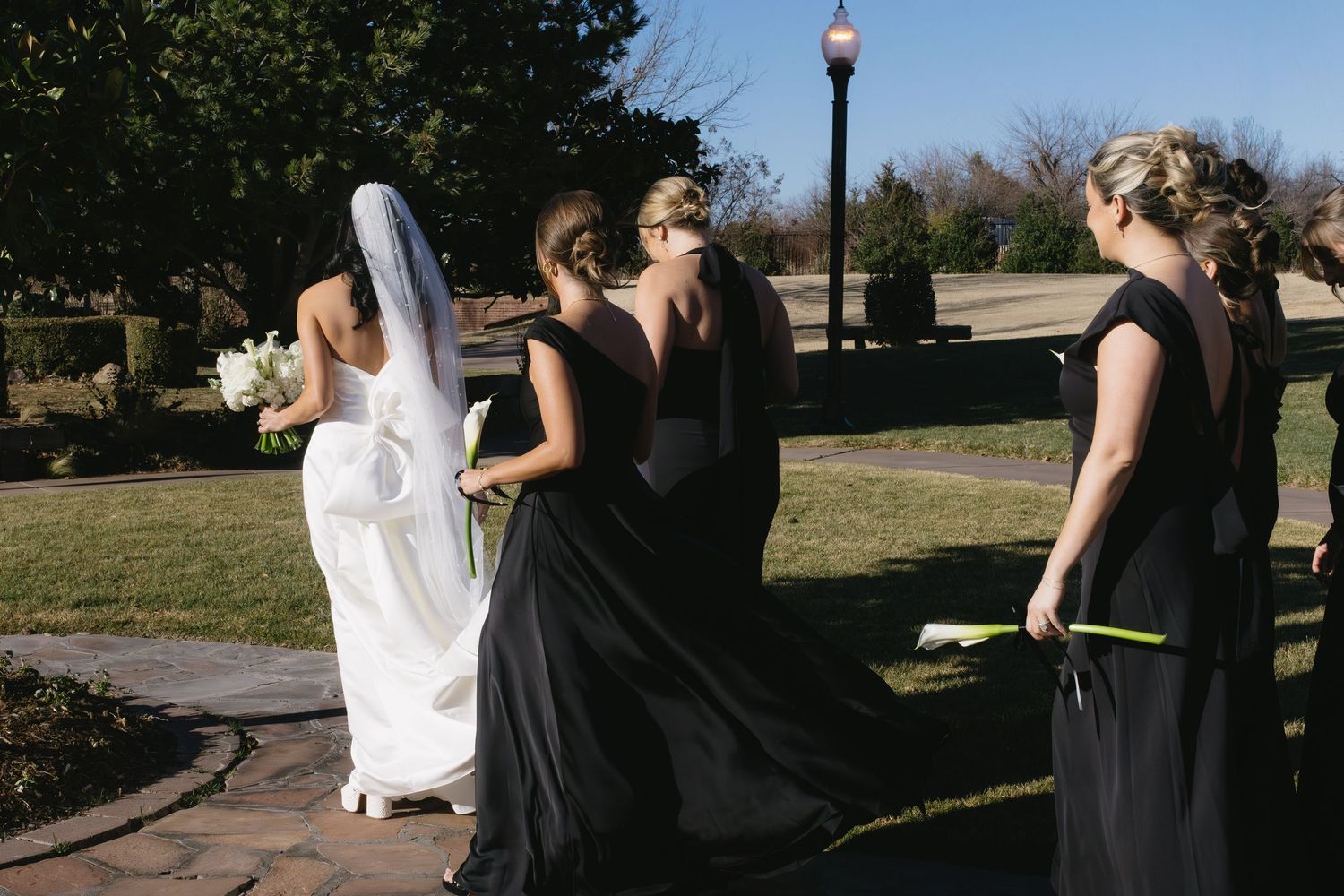 Wedding guests in black dresses outdoors with bride in white gown.