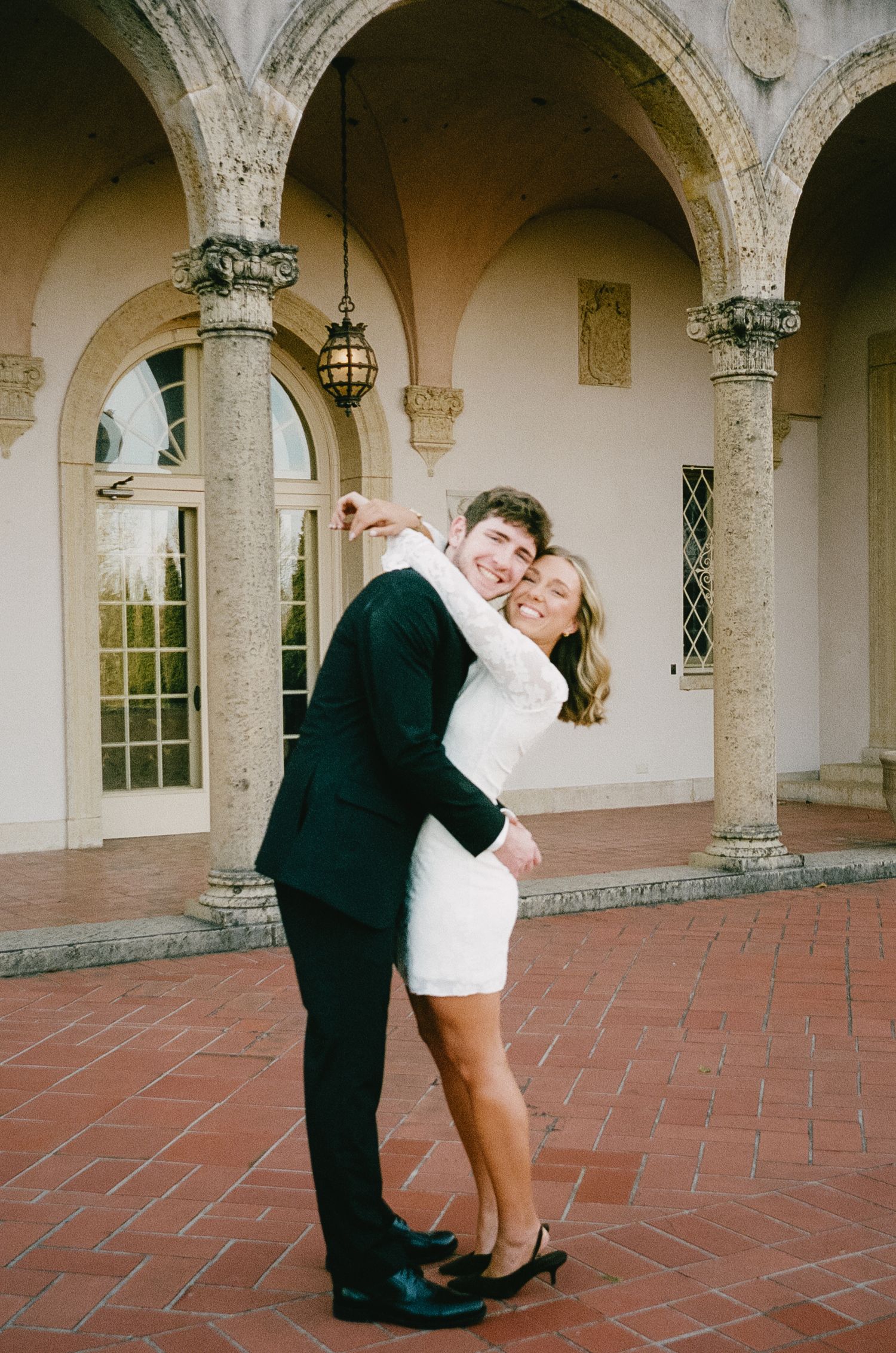 Couple dancing in an elegant arched colonnade with terracotta floors.