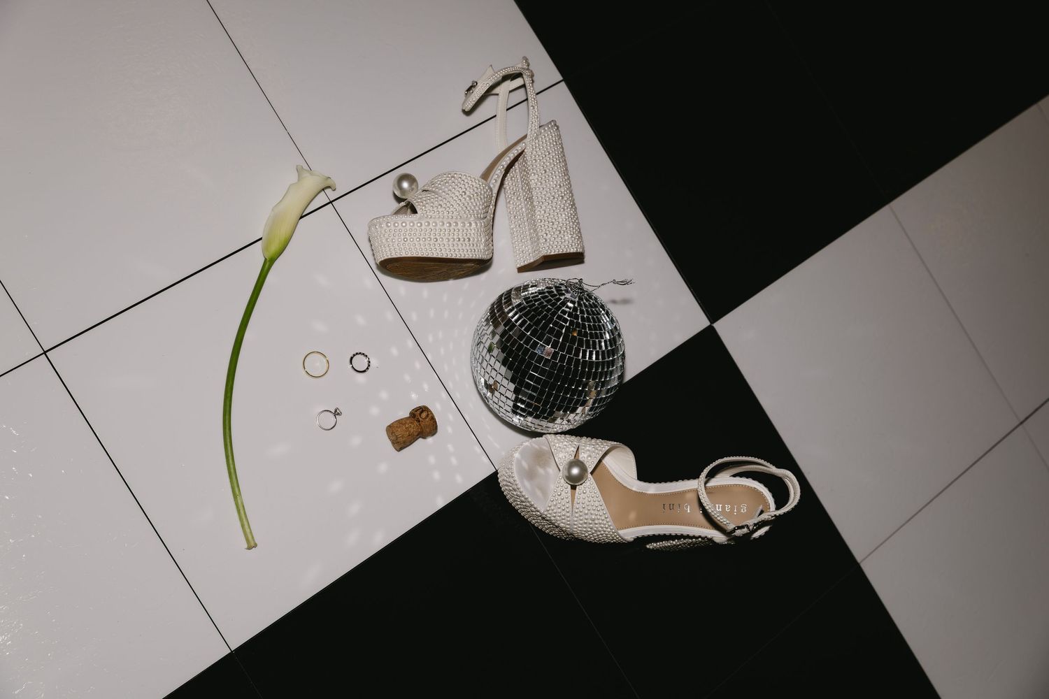 Elegant white heels and accessories arranged on a black and white geometric floor with a green stem accent.