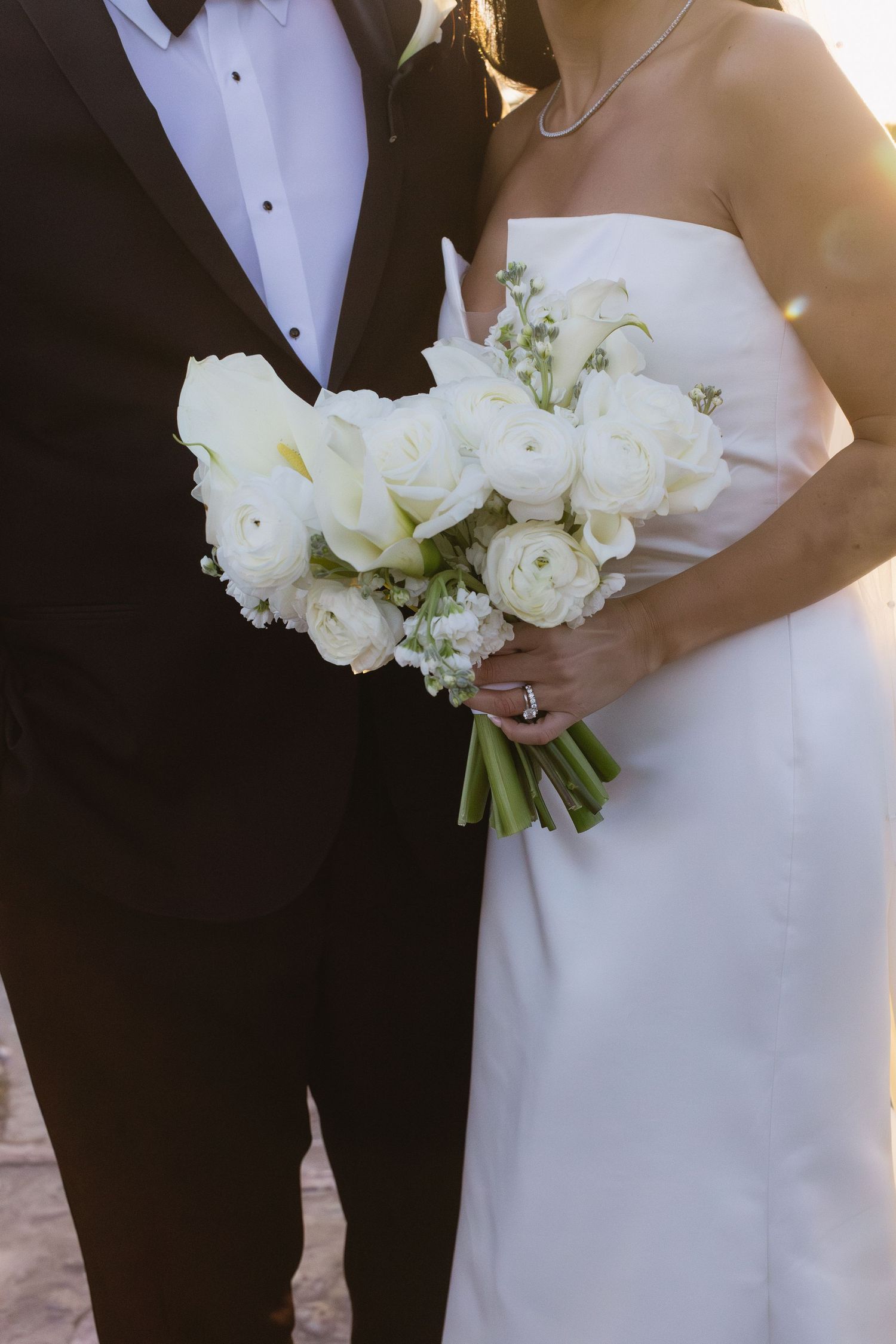 Close-up of couple with white rose bouquet showing wedding dress and tuxedo details.