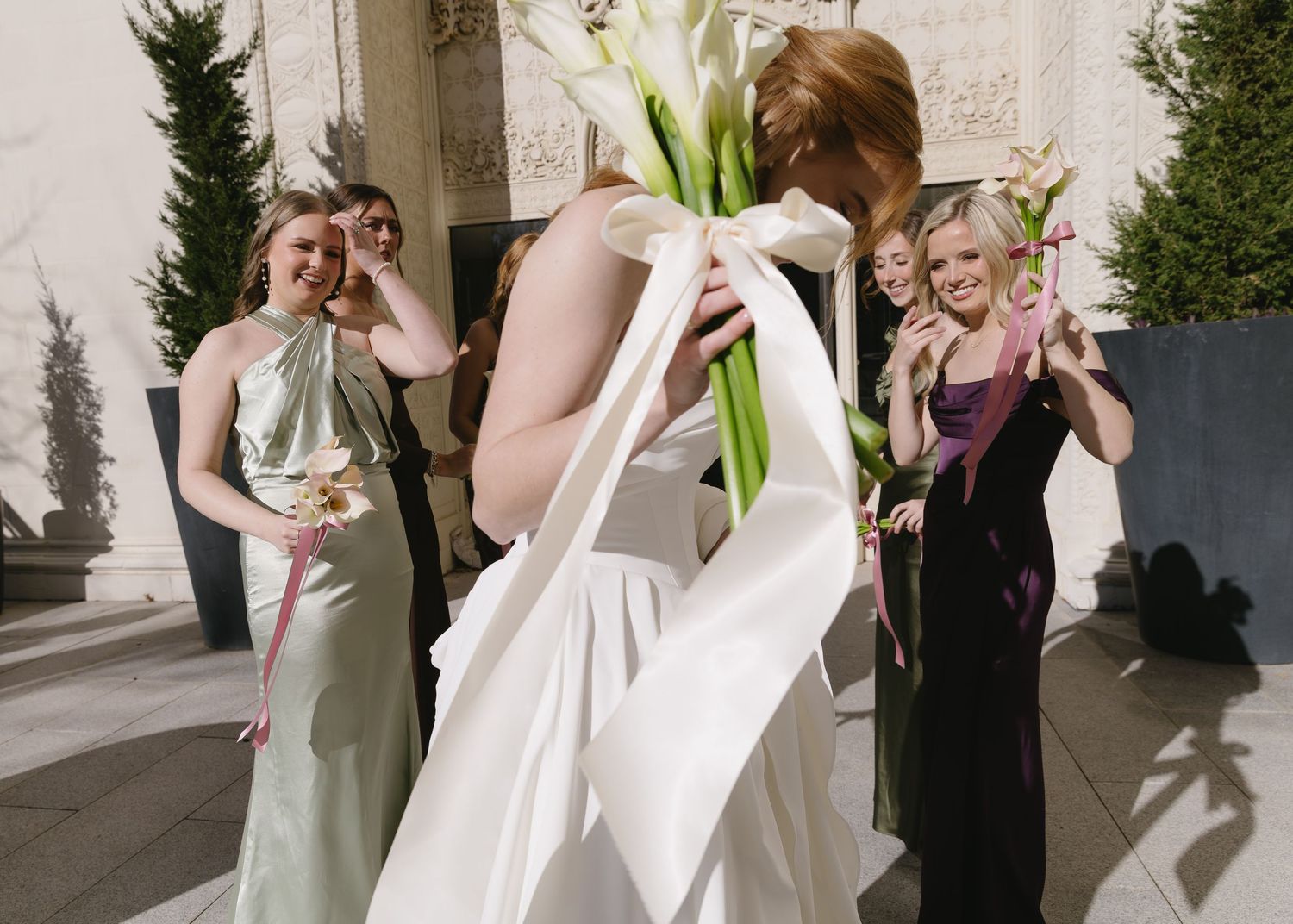 Wedding party members gather along a light-colored stone wall for formal photos.