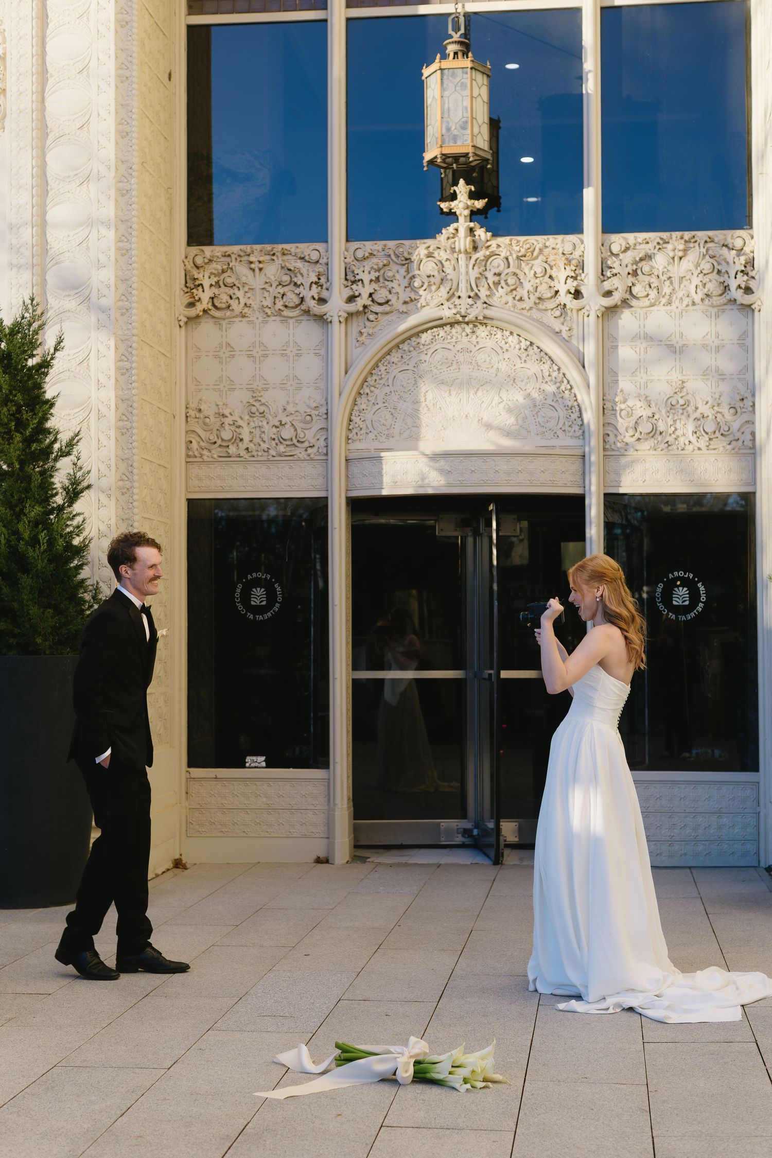 Newlyweds share romantic moments outside modern building with large glass windows and stone facade.