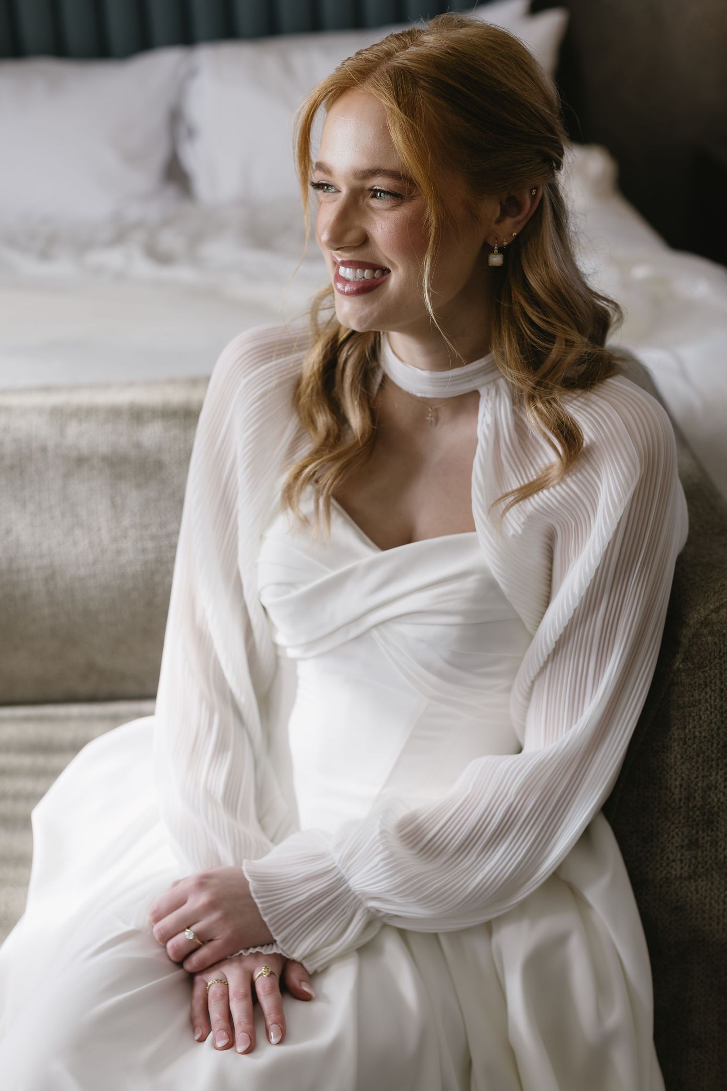 A bride in an elegant white gown with billowing sleeves poses on a light colored sofa.