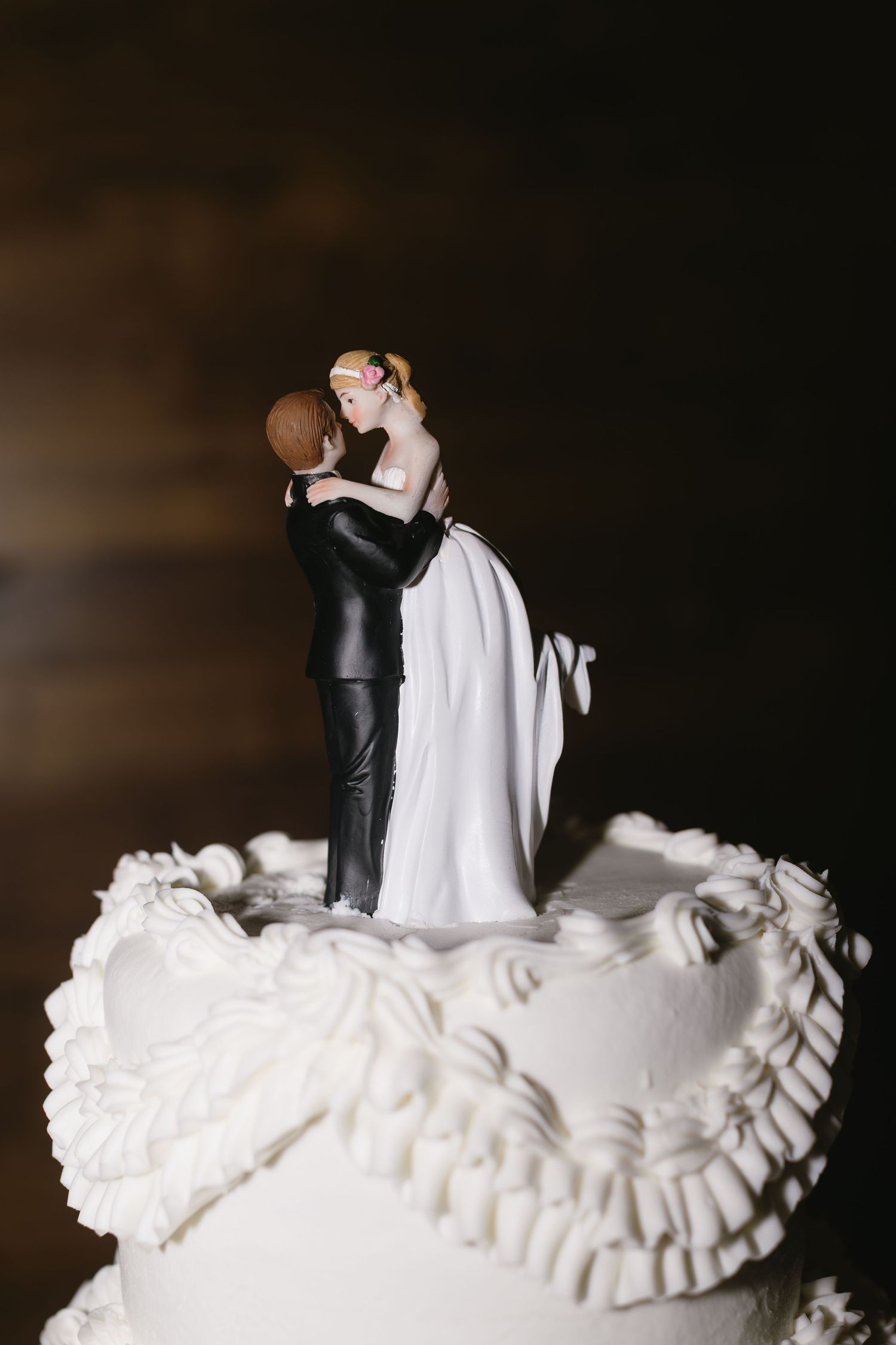 White wedding cake topper figurines with ruffled details against dark background.