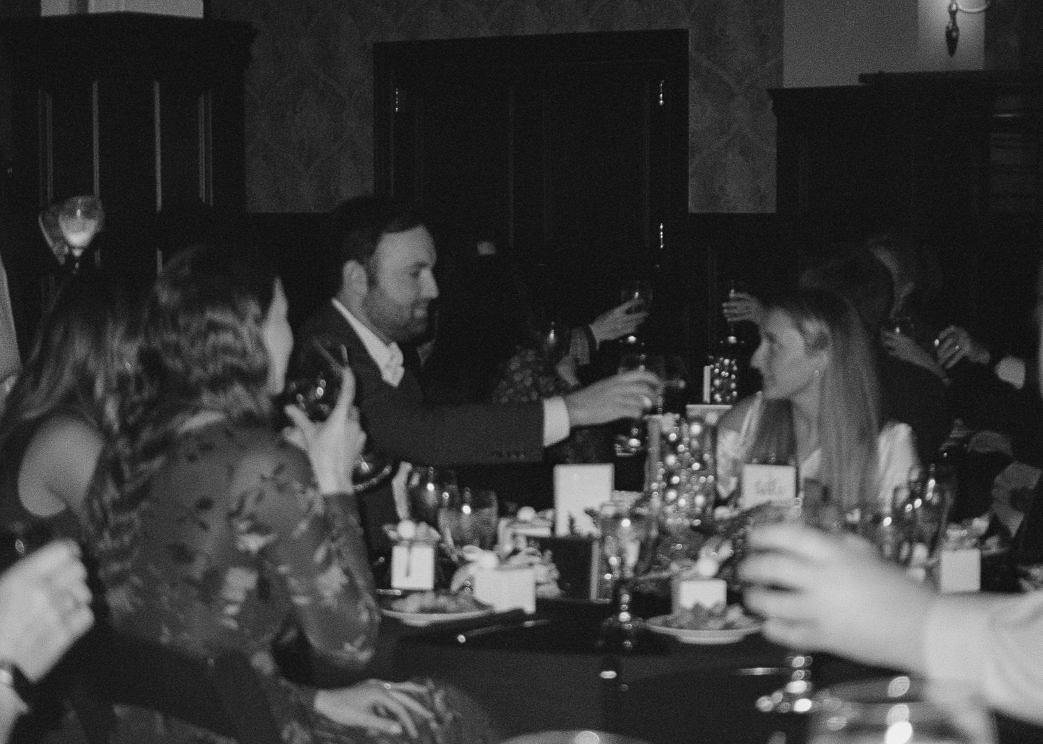 Dark monochrome photograph of people gathered at tables in a dimly lit venue.