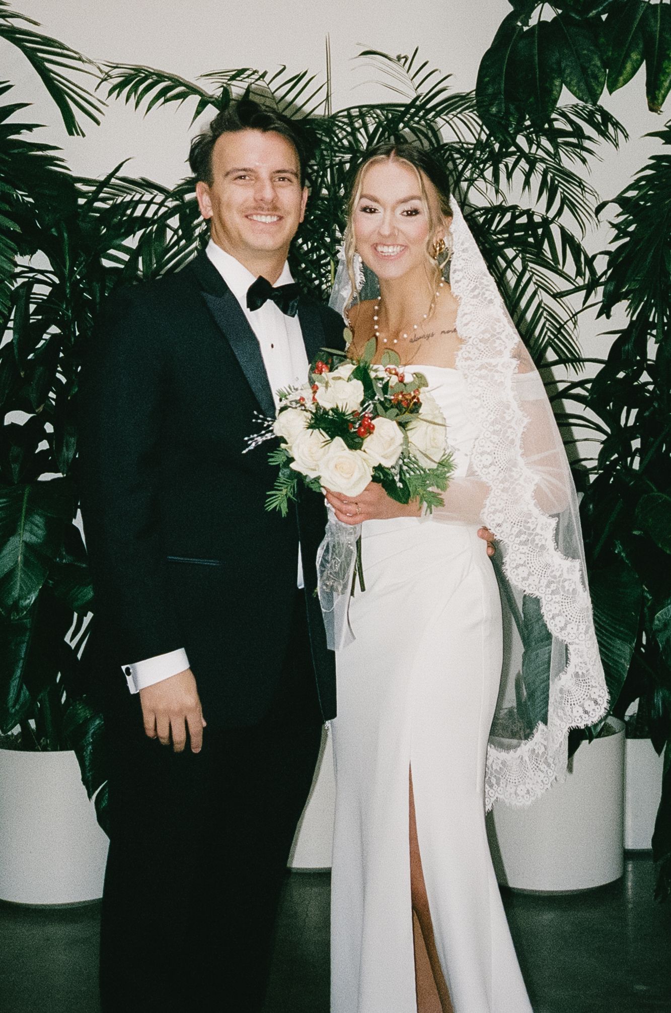 Wedding couple poses against tropical greenery backdrop.
