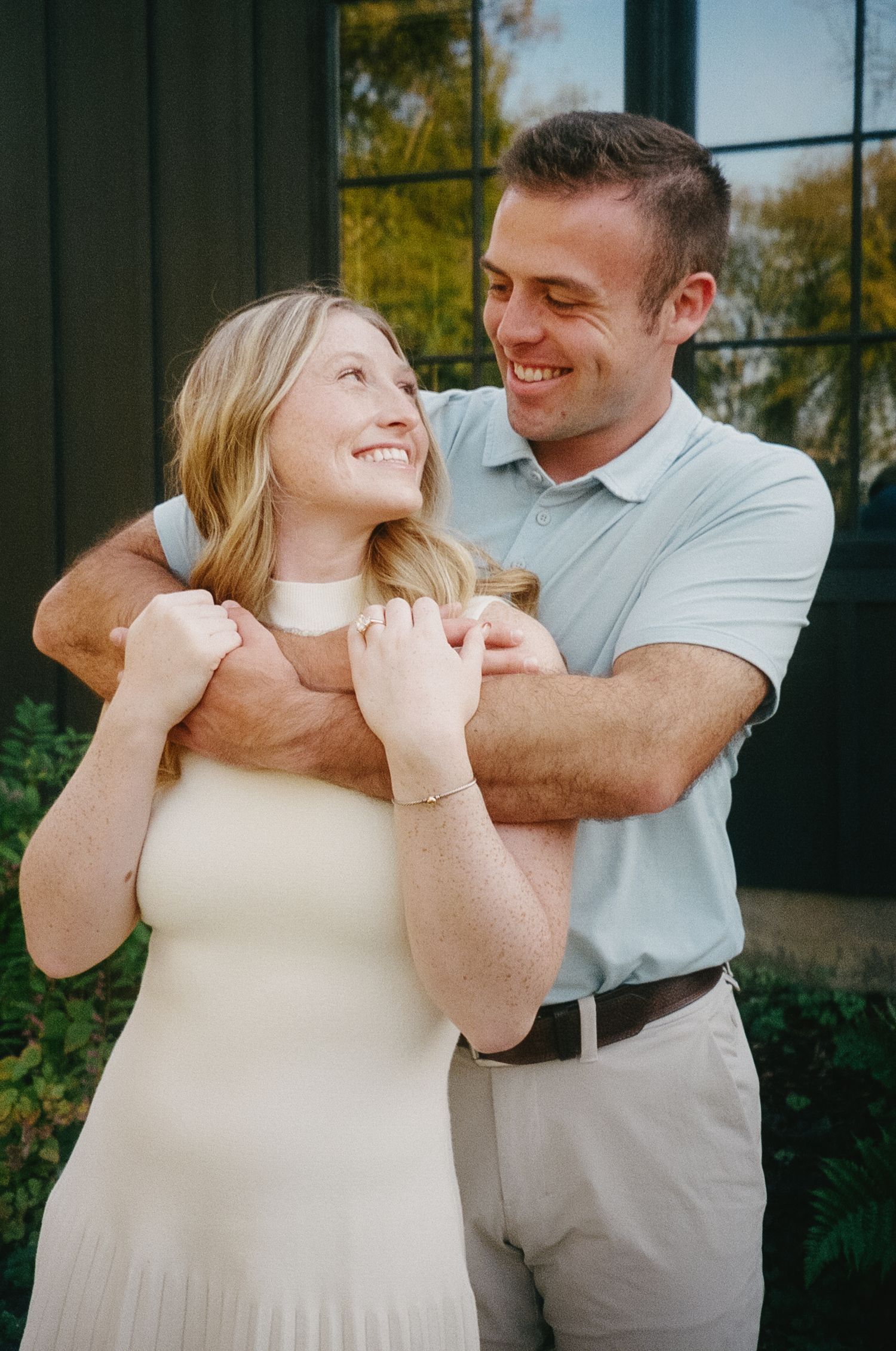 A couple shares a joyful moment together outdoors while embracing and laughing in casual attire.