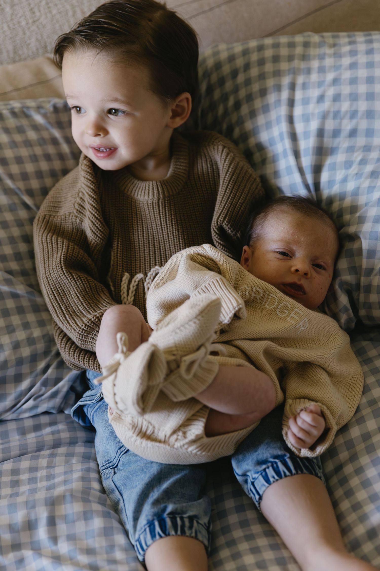 Sweet interaction between siblings on blue and white checkered bedding.