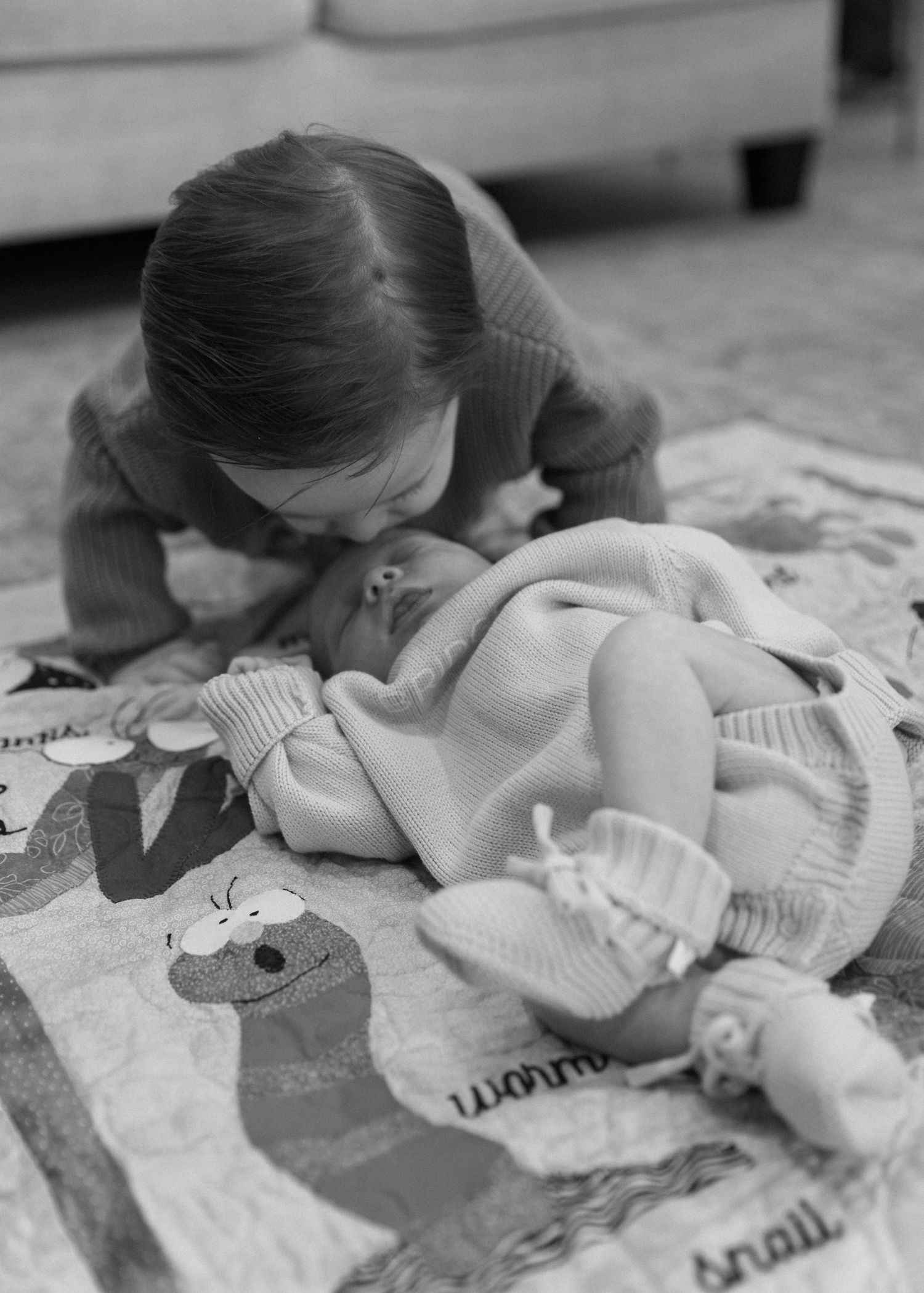 A child leans down to interact with a baby doll laid out on a play mat with text patterns.