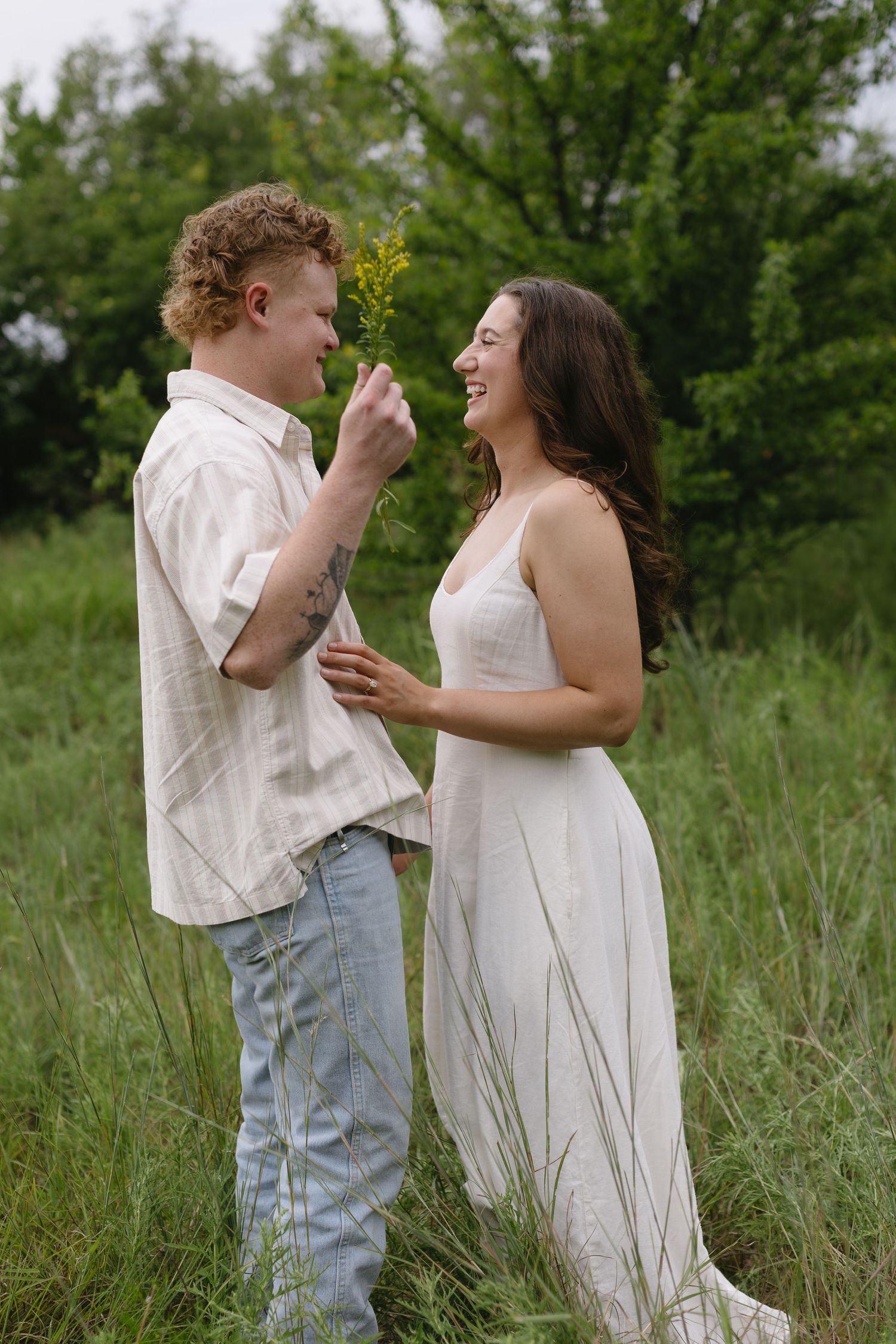 A couple in white clothing shares tender moments while standing in tall grass on a summer day.