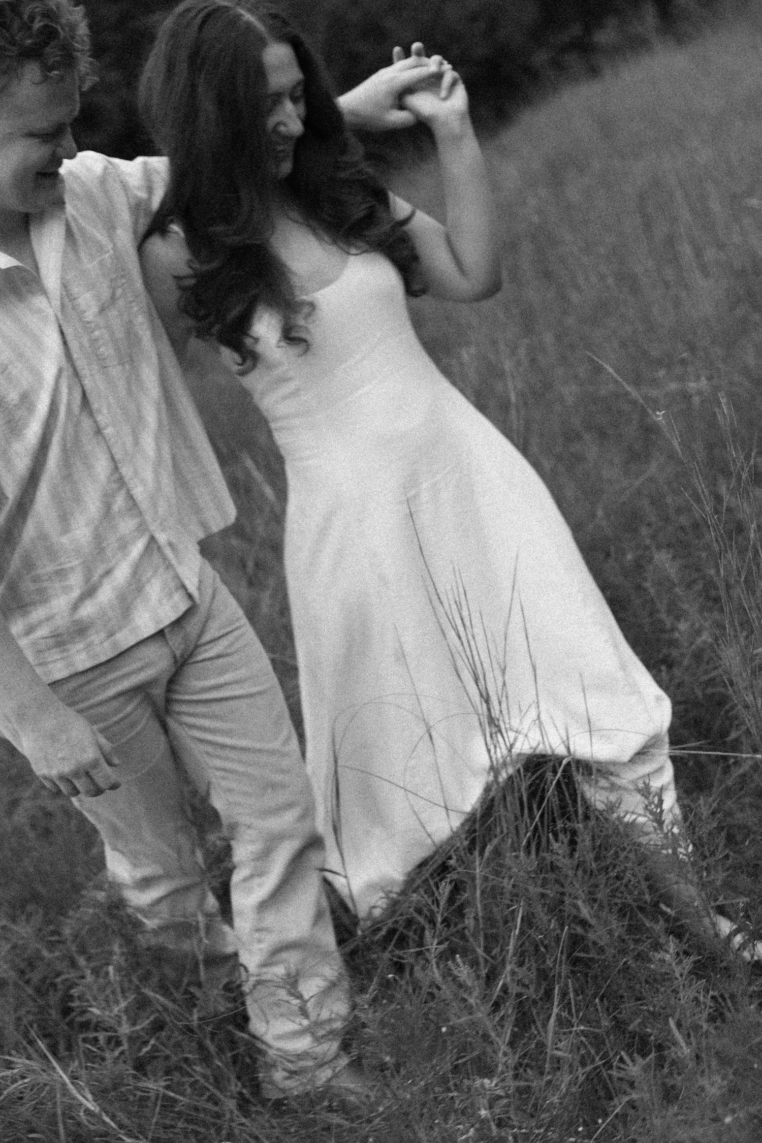 A black and white photo captures an intimate moment between two people in a grassy field.