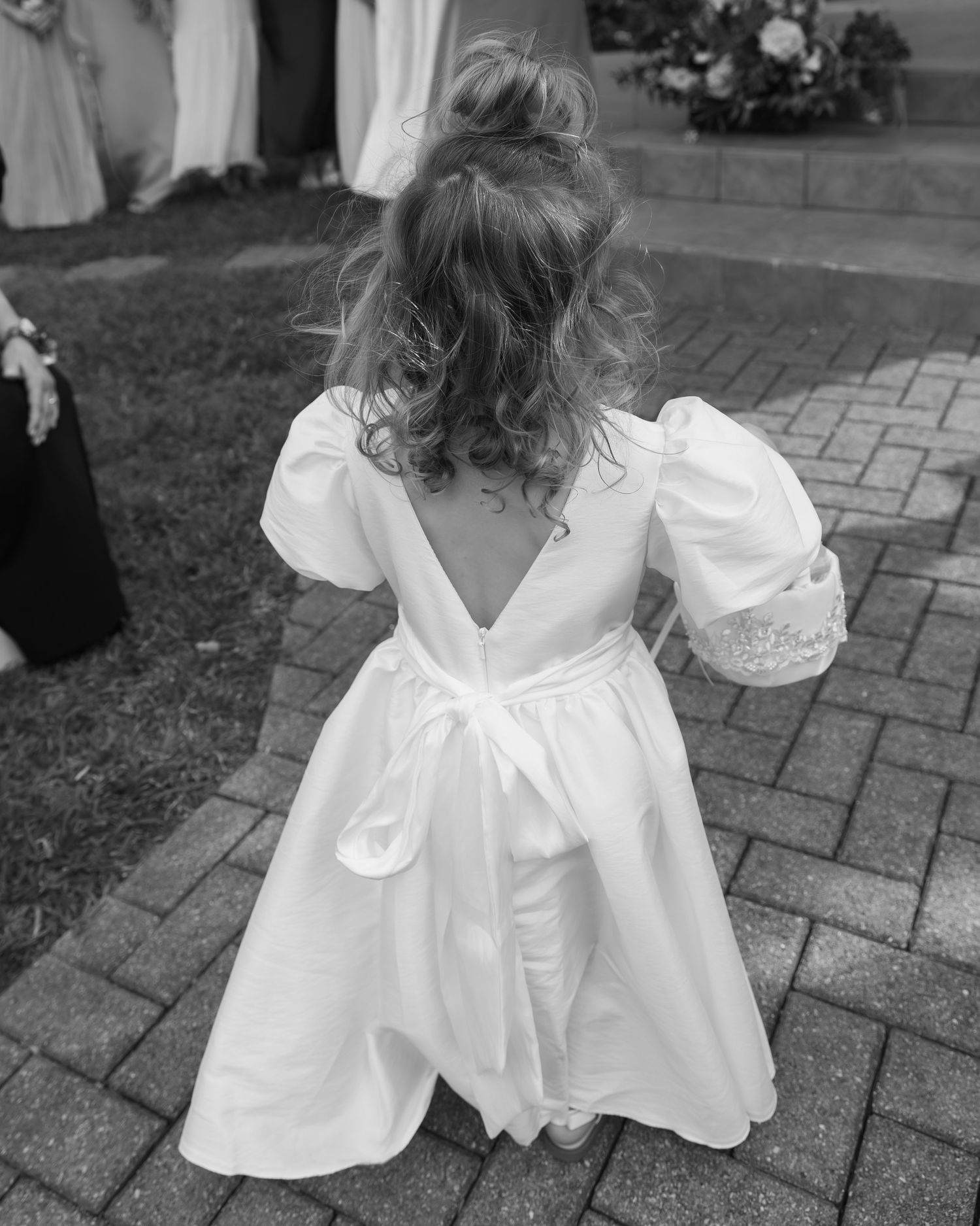 Close-up view of a white ruffled flower girl dress detail on brick pavement.