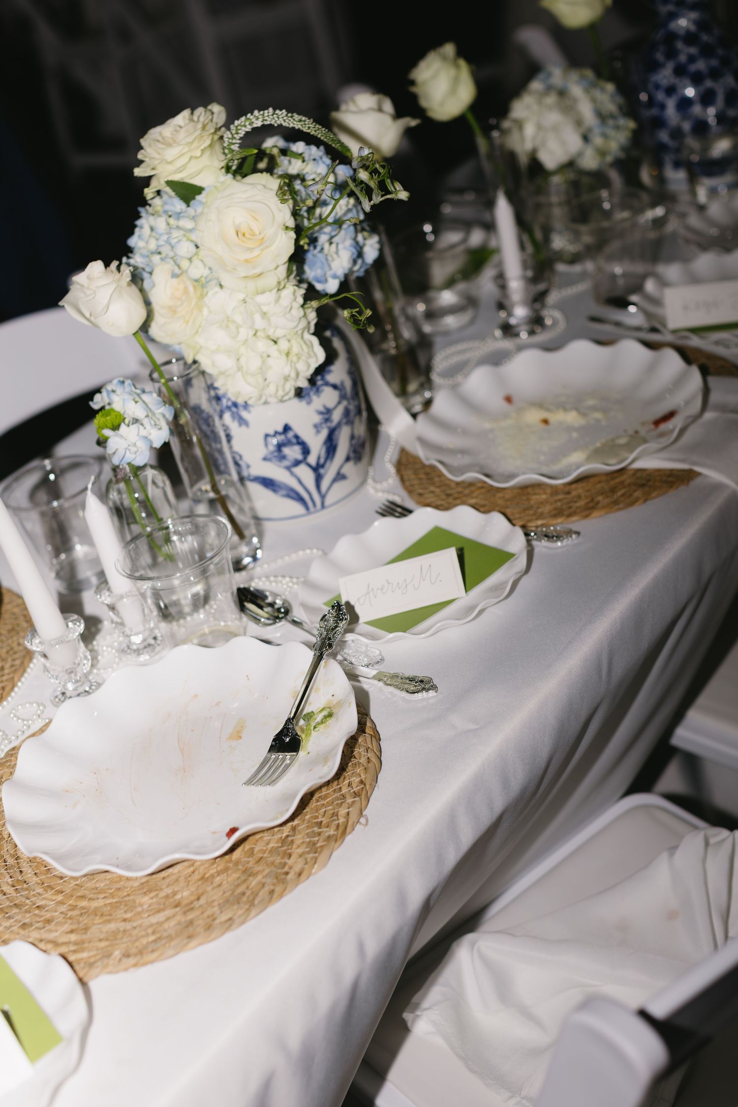 Wedding reception table decorated with blue and white porcelain vases and white floral centerpieces.