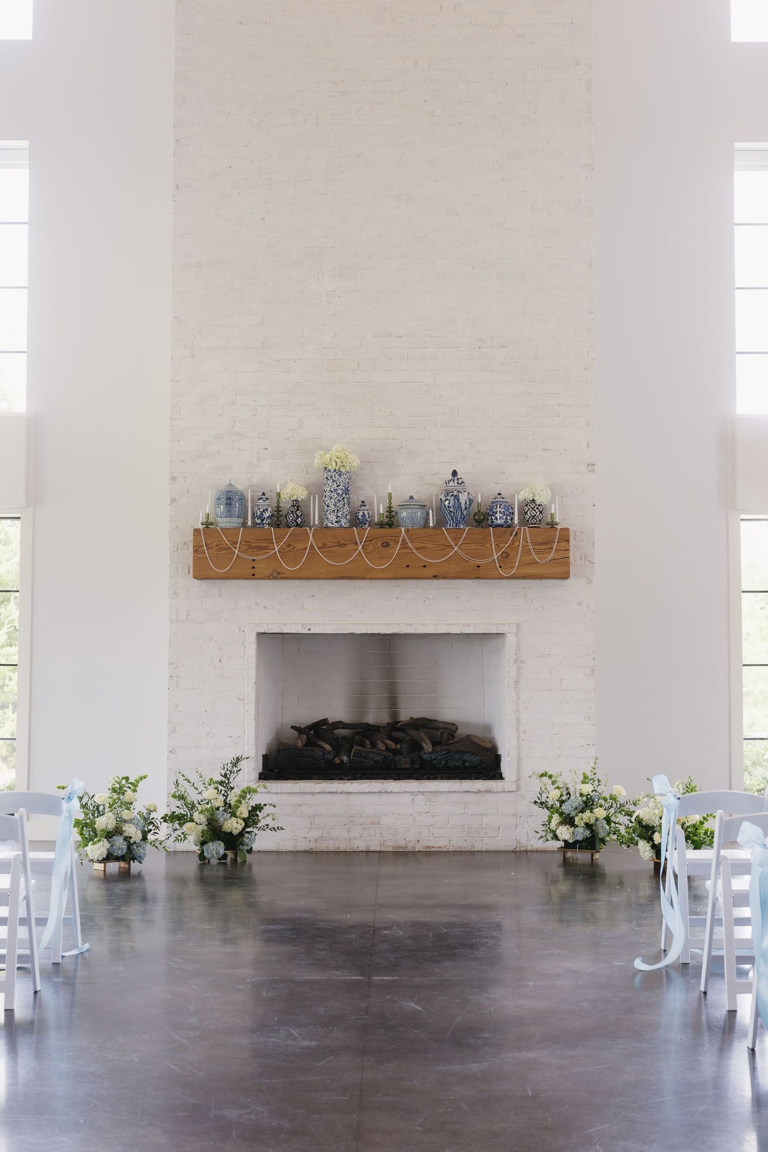 Modern white wedding venue with rustic wooden shelf and floral decorations.