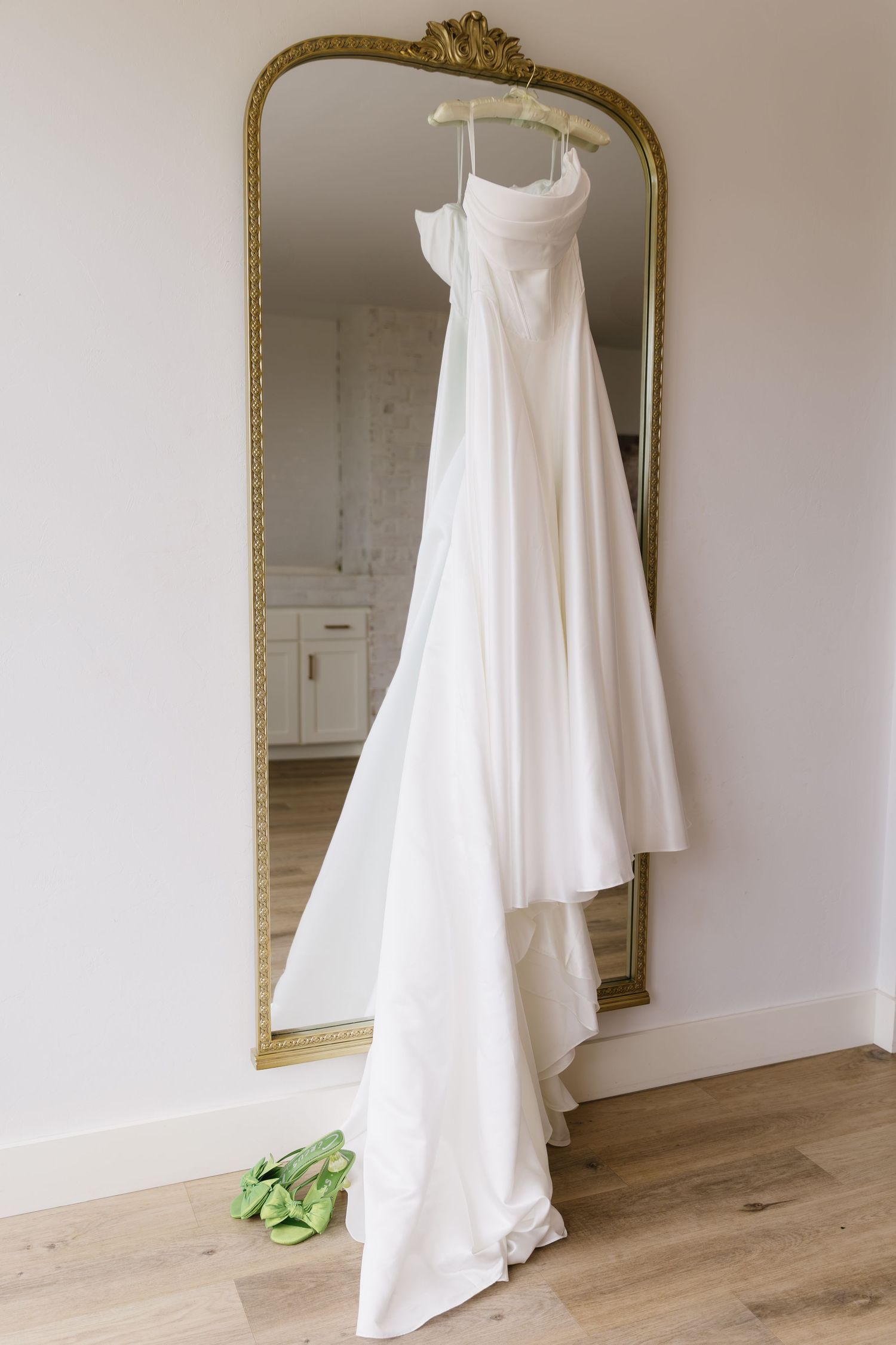 Elegant white wedding dress hanging on a gold-framed mirror against a minimalist white wall.