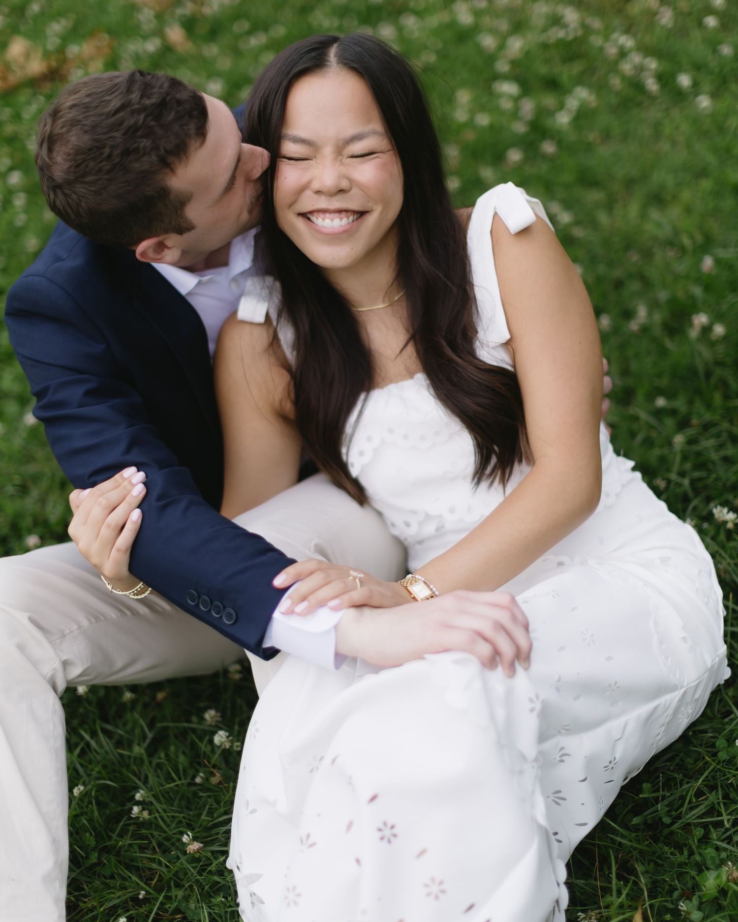 A couple shares intimate moments while sitting together on grass with white flowers blooming nearby.