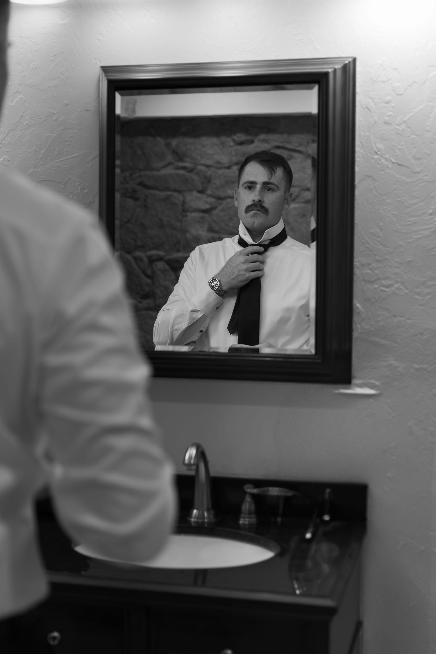 Black and white reflection of person adjusting tie in bathroom mirror.
