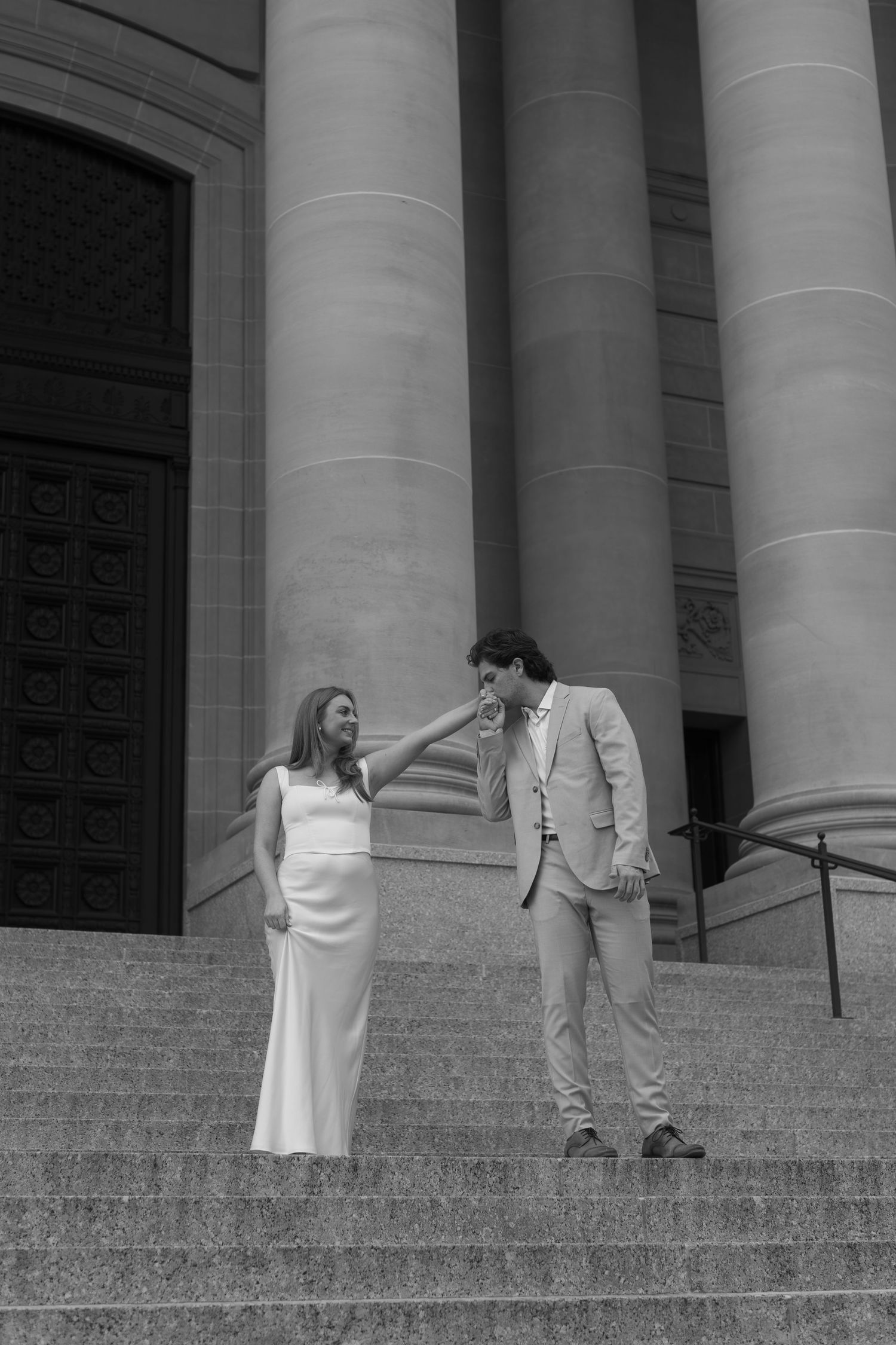 A couple in formal attire ascending stone steps with large columns in the background.