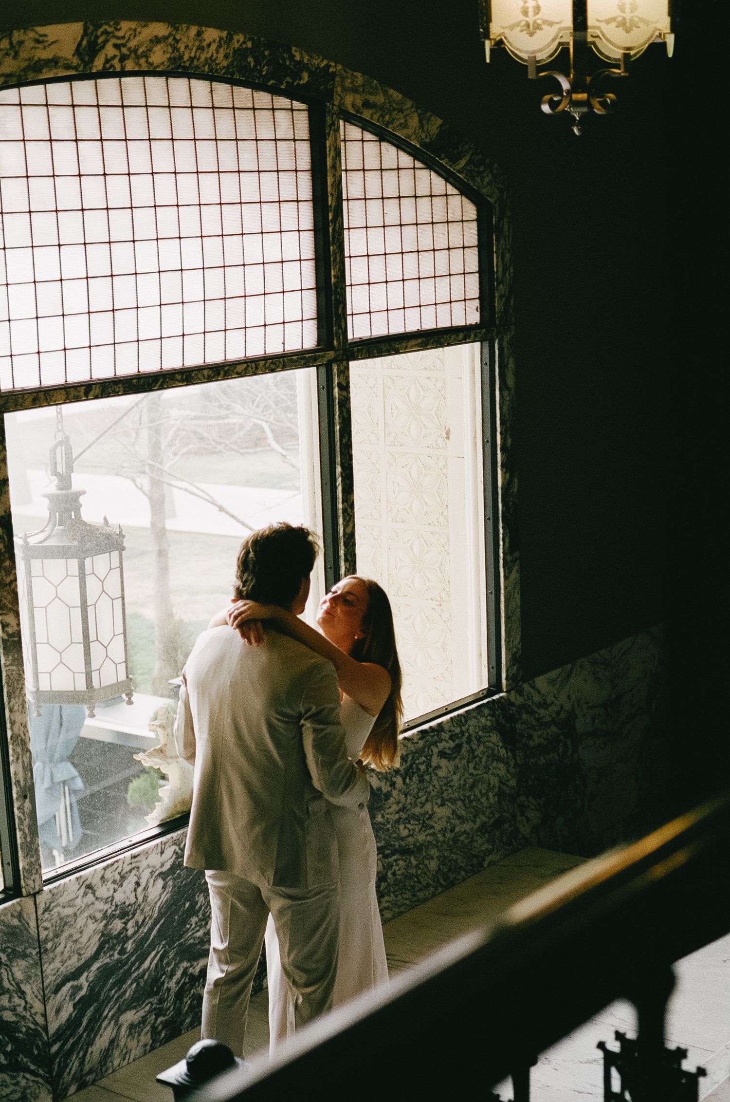 Silhouetted couple in formal wear looking through large vintage windows.