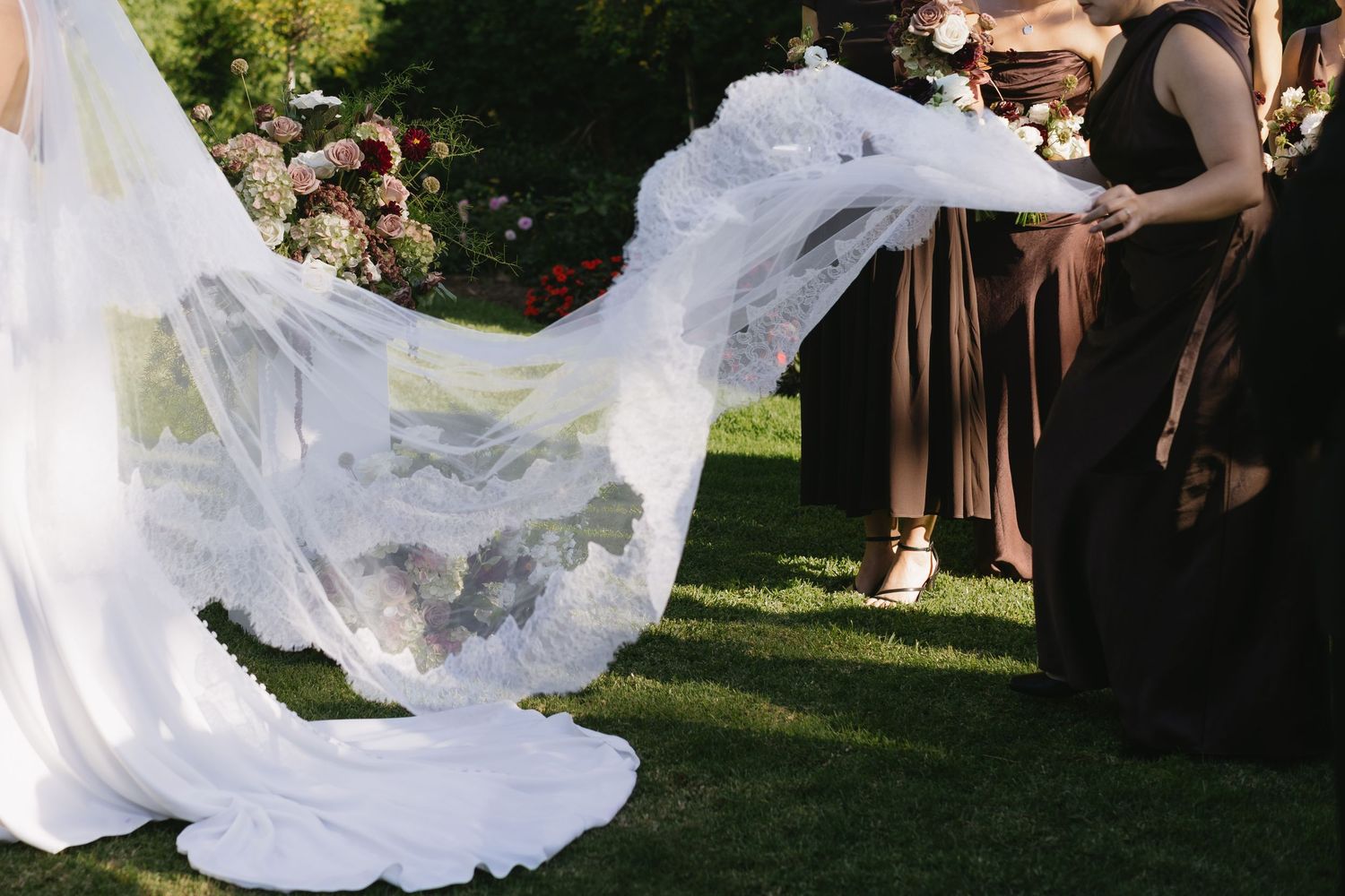 Flowing white wedding dress train billows dramatically in outdoor garden setting.
