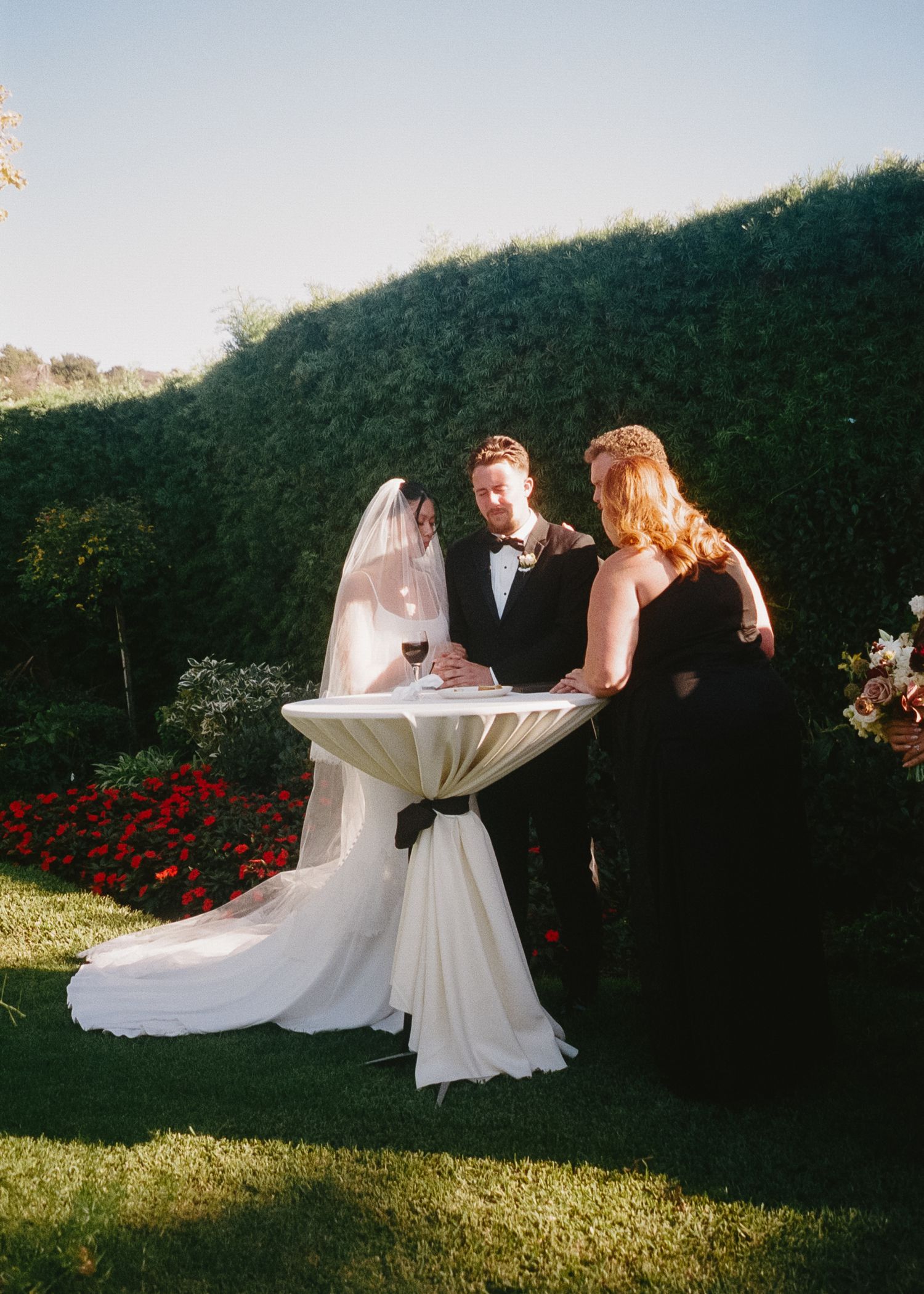 Wedding ceremony signing moment at outdoor garden table with floral backdrop.