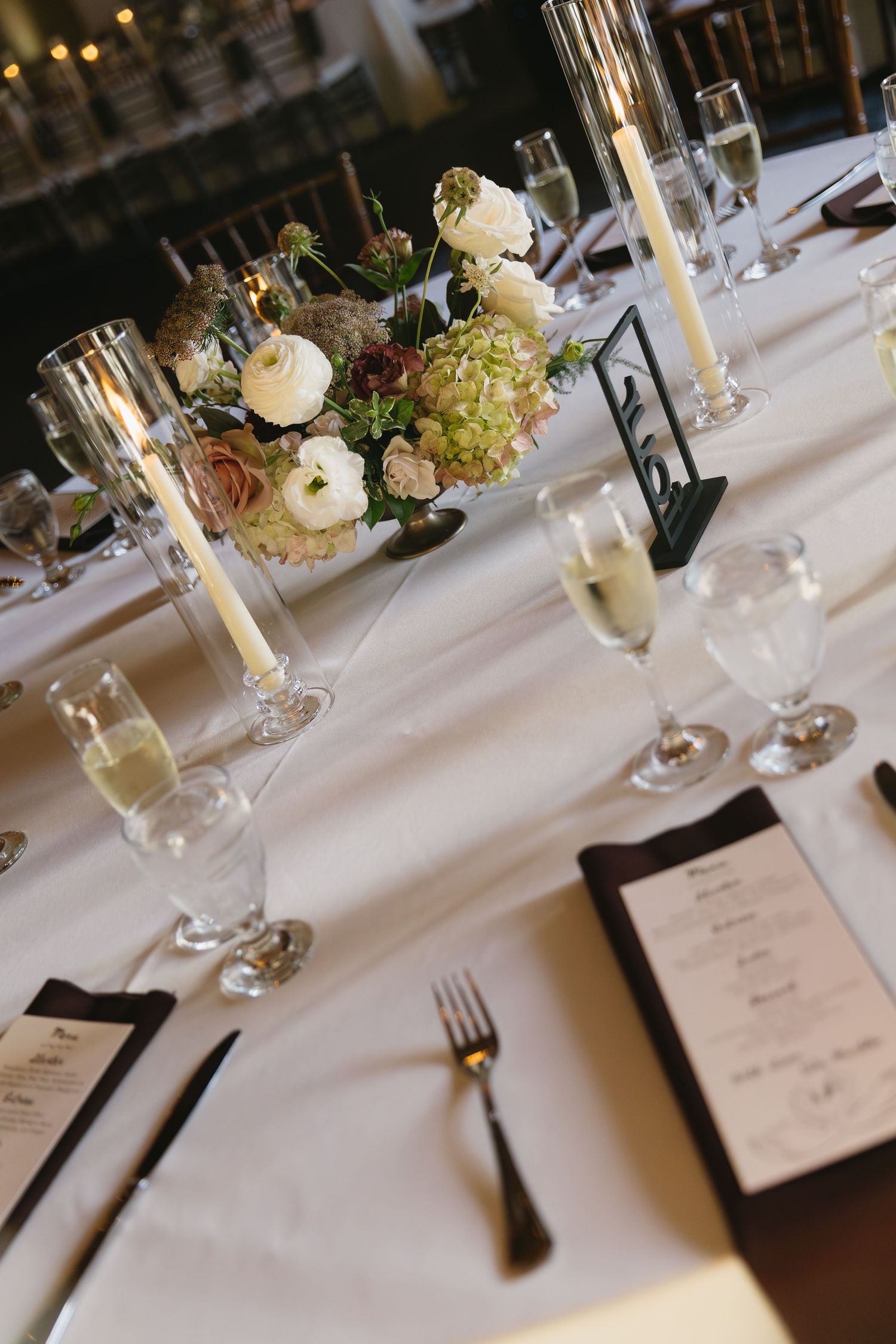 Wedding table setting with floral centerpiece, champagne glasses, and menu cards on white linens.