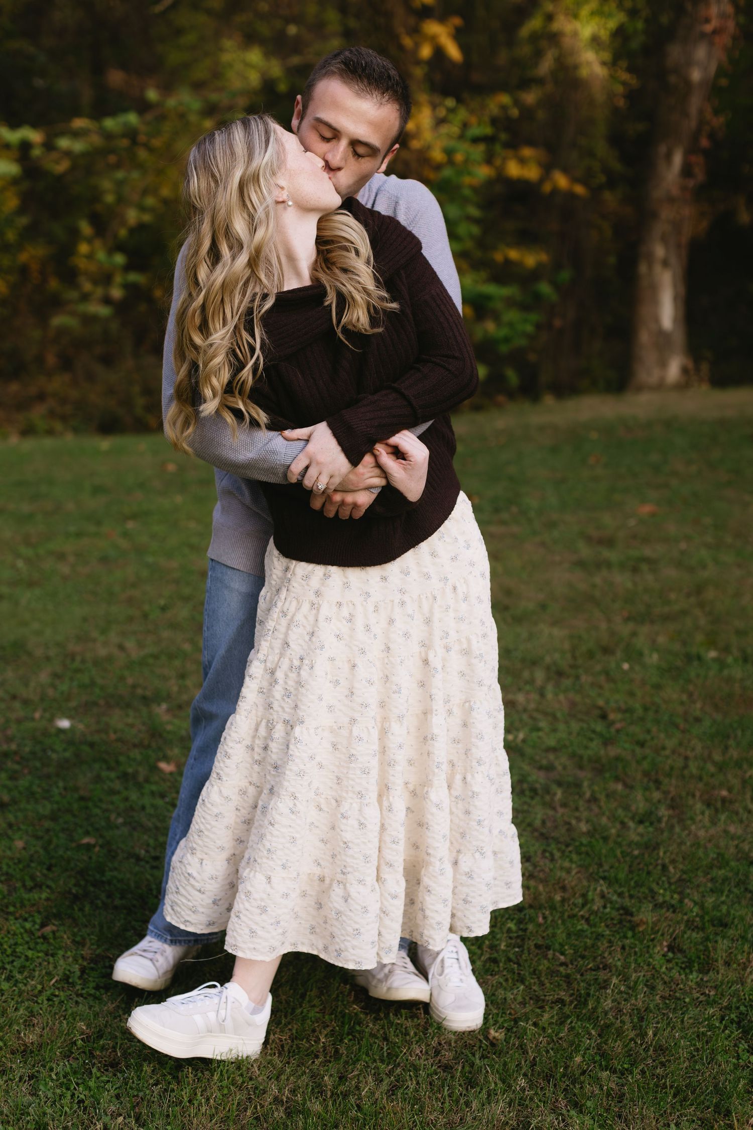 Couple in casual attire sharing intimate moments on grass during outdoor photoshoot.