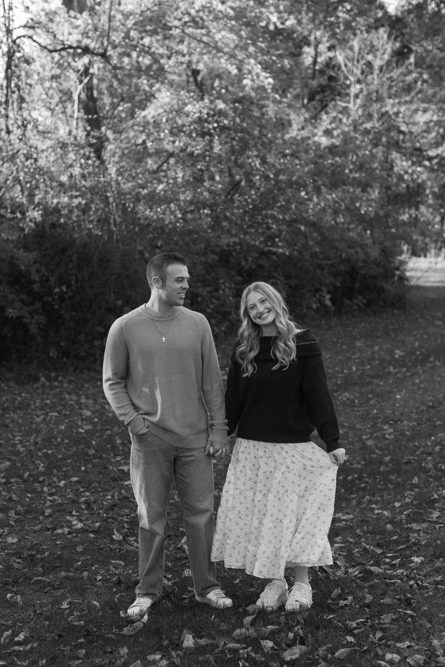 A couple sits together on grass during autumn with trees in the background.