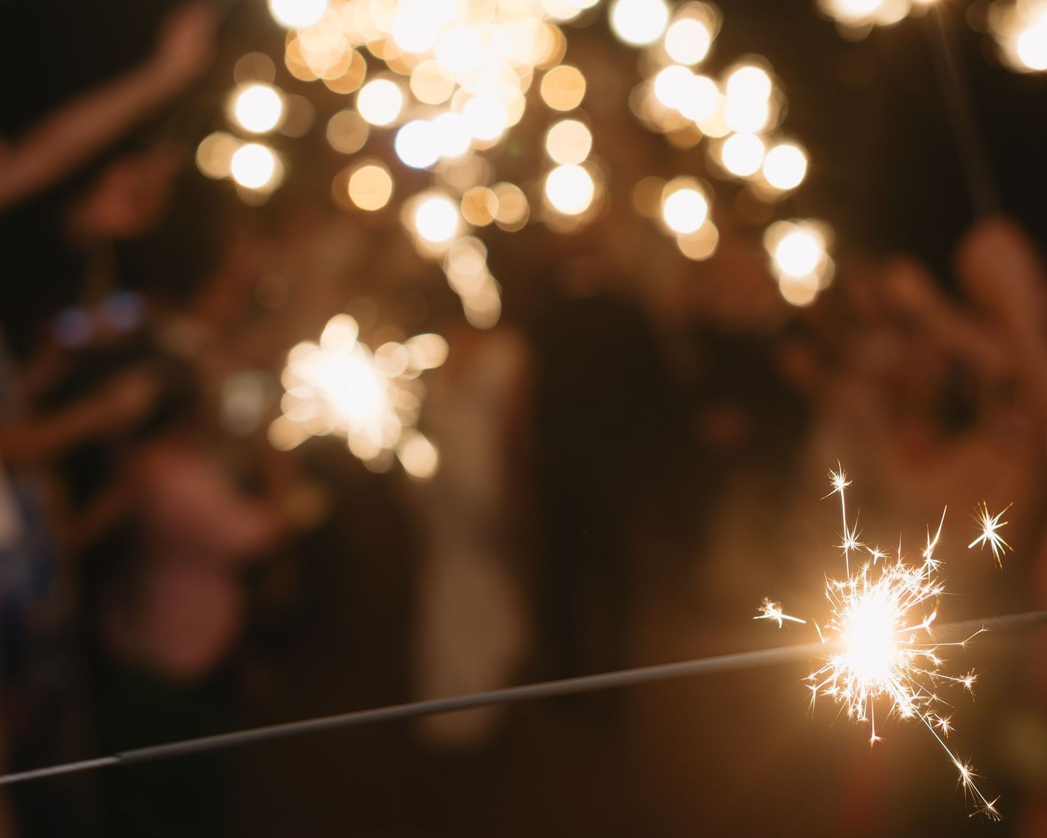 Sparklers create magical light trails against dark night sky at wedding celebration.