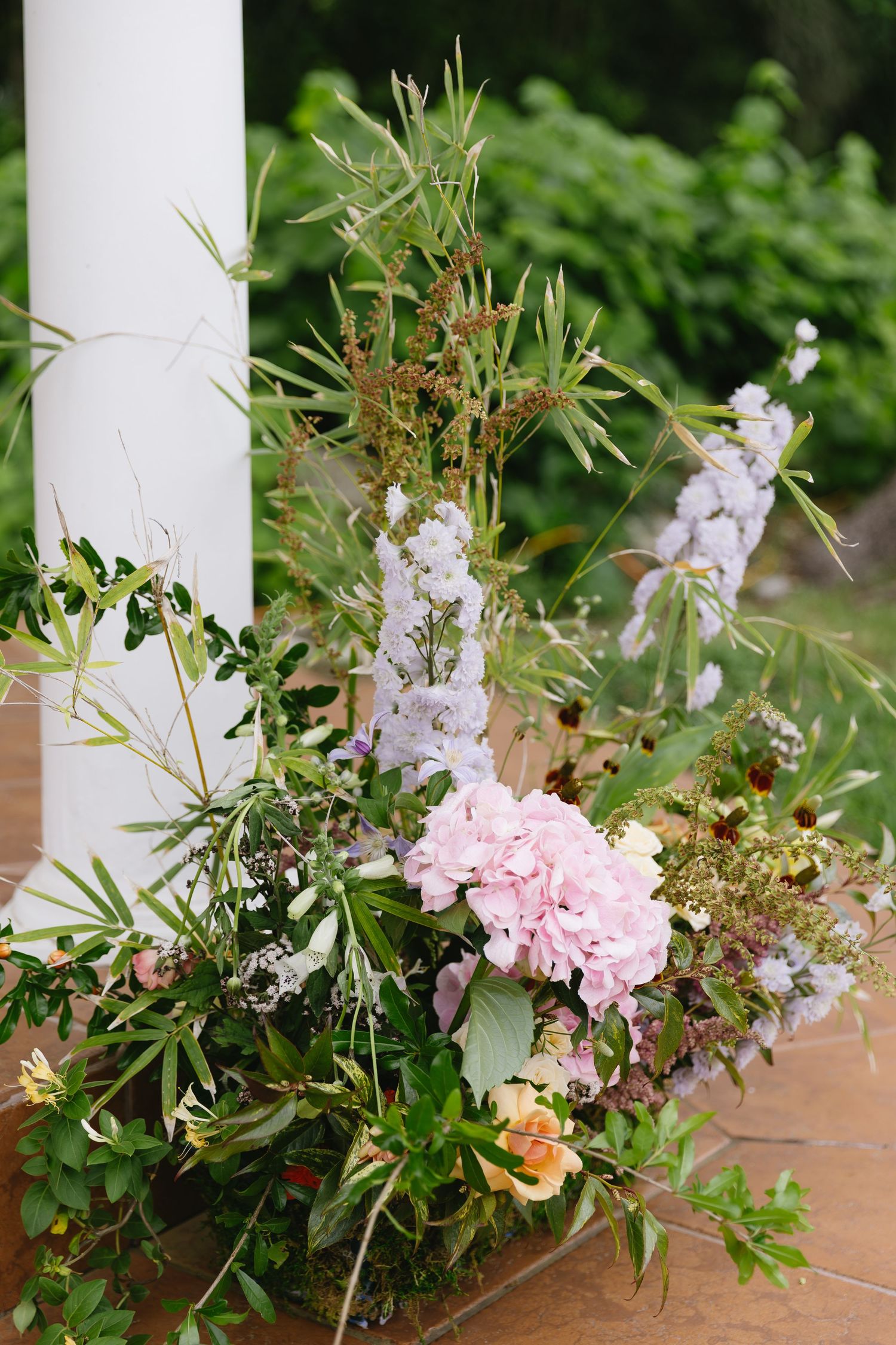 Garden-style floral arrangement with pink peonies and delicate white blooms against white column.